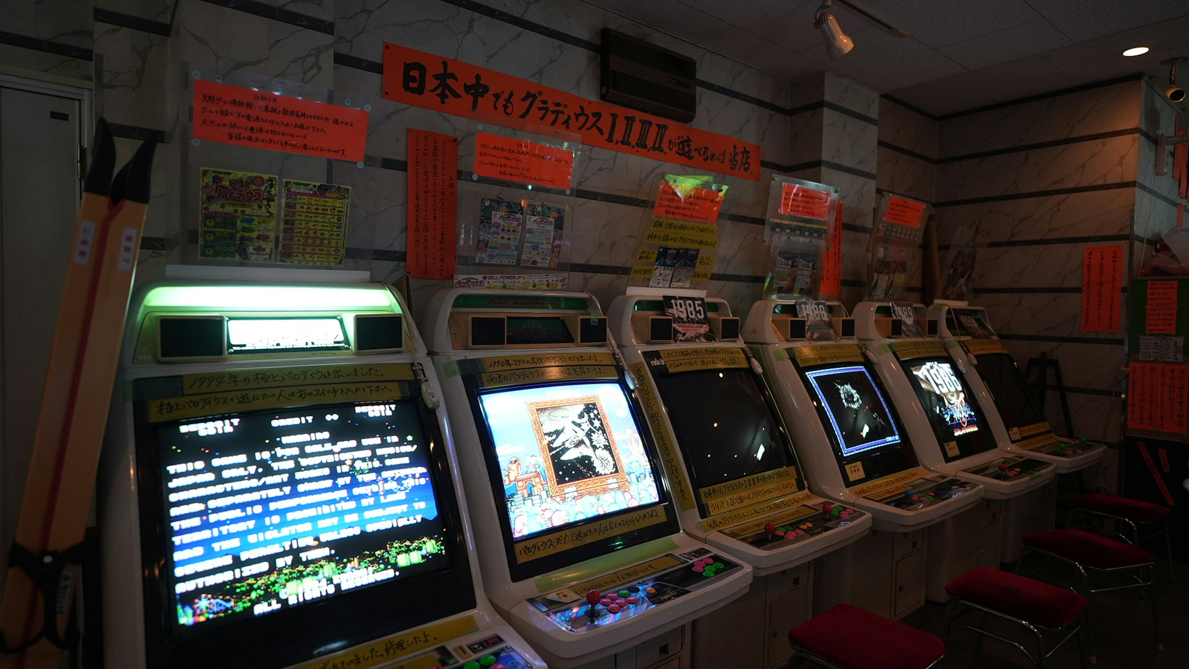 暗い部屋に並ぶゲーム機の列と明るいモニター