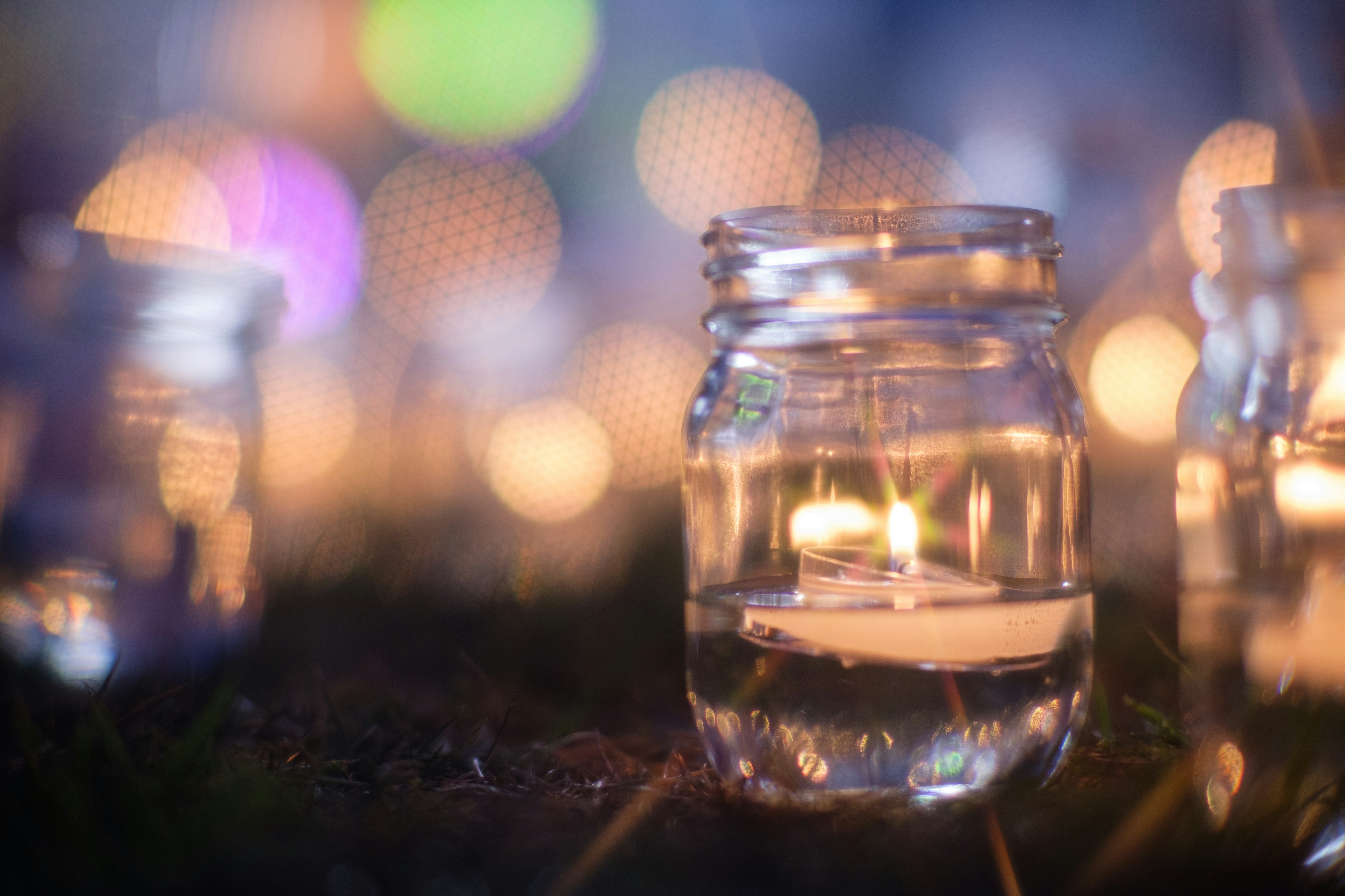 A glass jar with a candle placed on grass in a nighttime setting