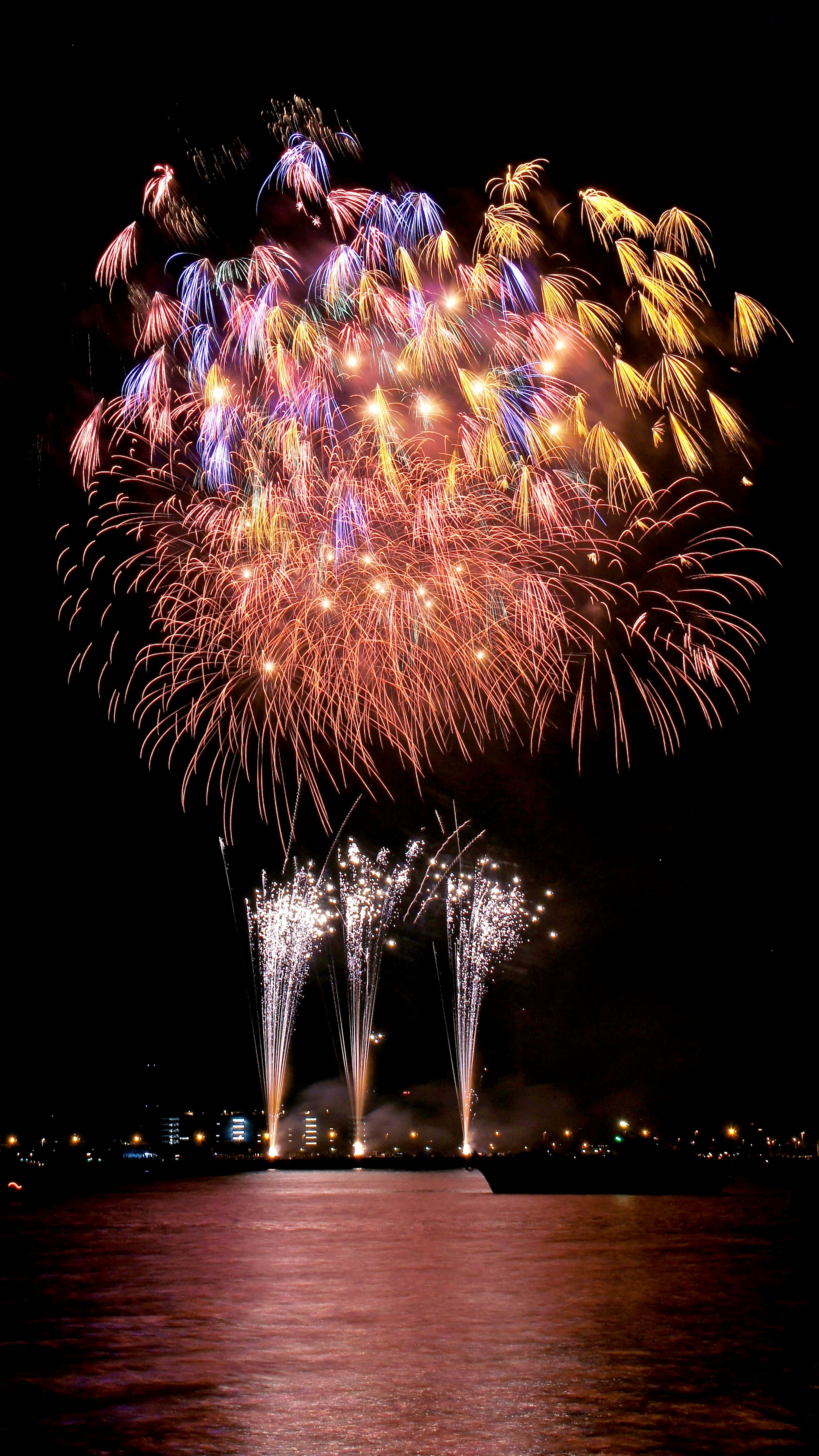 Spettacolo di fuochi d'artificio colorati che illumina il cielo notturno riflessi sull'acqua