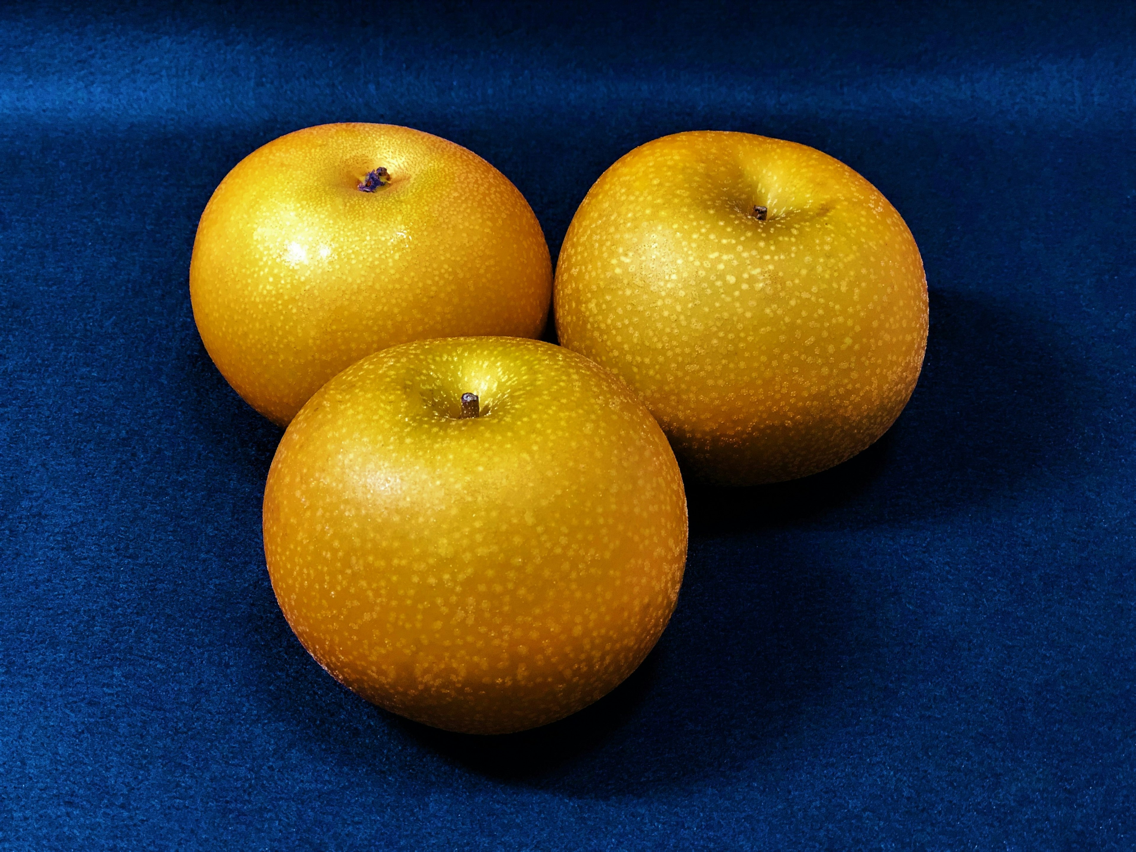 Three orange fruits placed on a blue fabric background