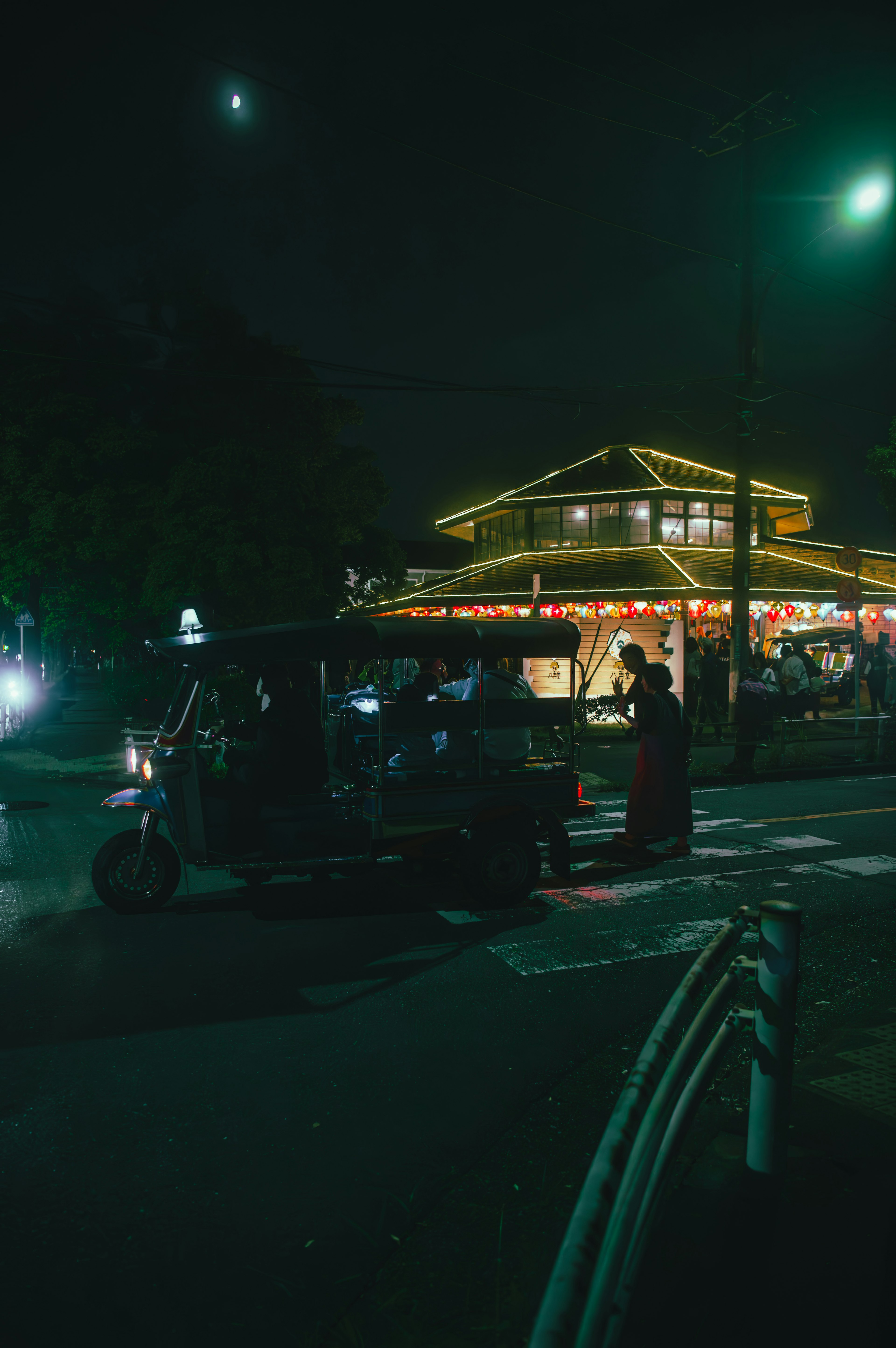 Scena notturna con un tuk-tuk fermo all'angolo di una strada Edificio illuminato e luci dei veicoli visibili