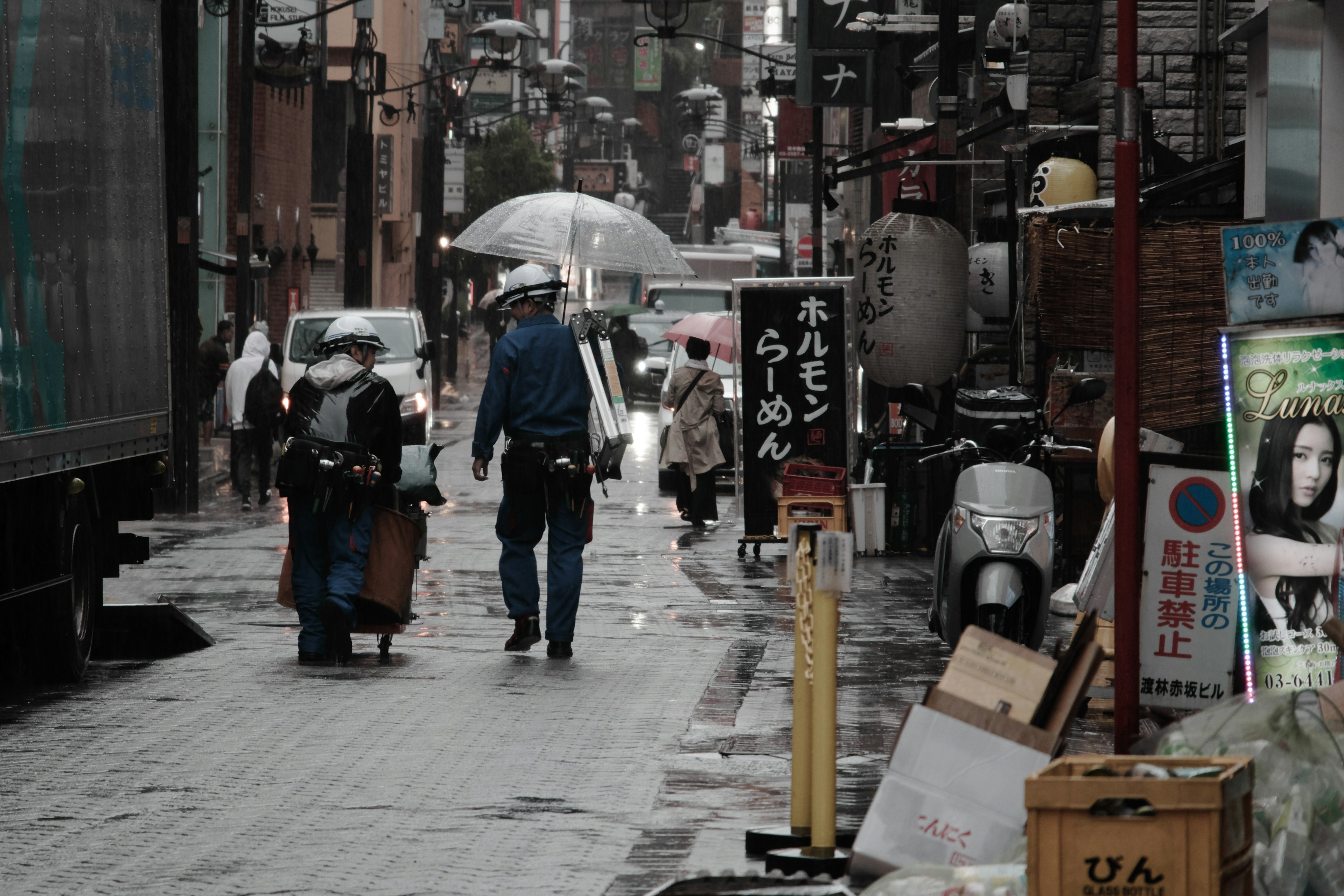 雨の中の狭い通りを歩く人々と傘