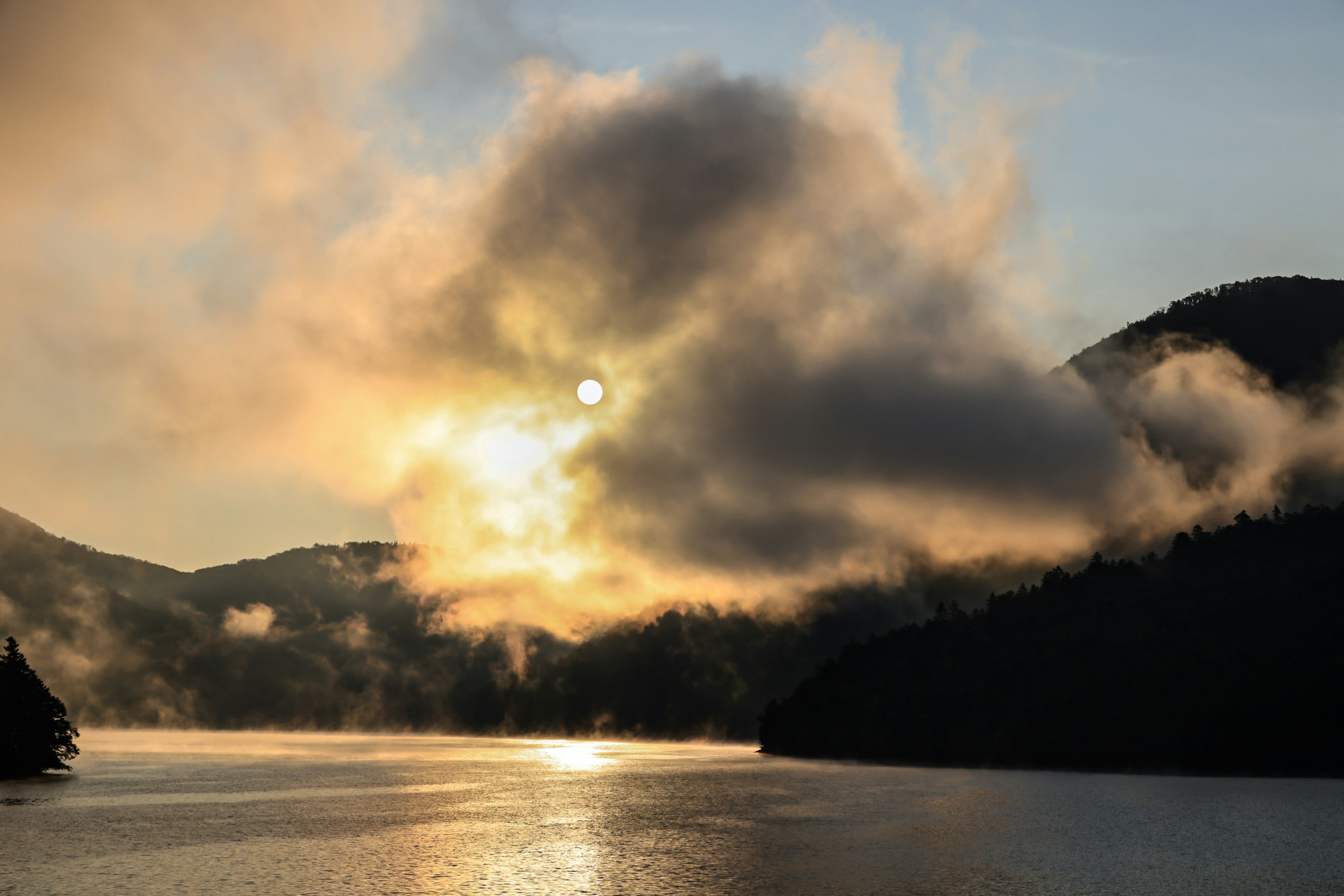 霧に包まれた湖に沈む太陽と山々の美しい風景