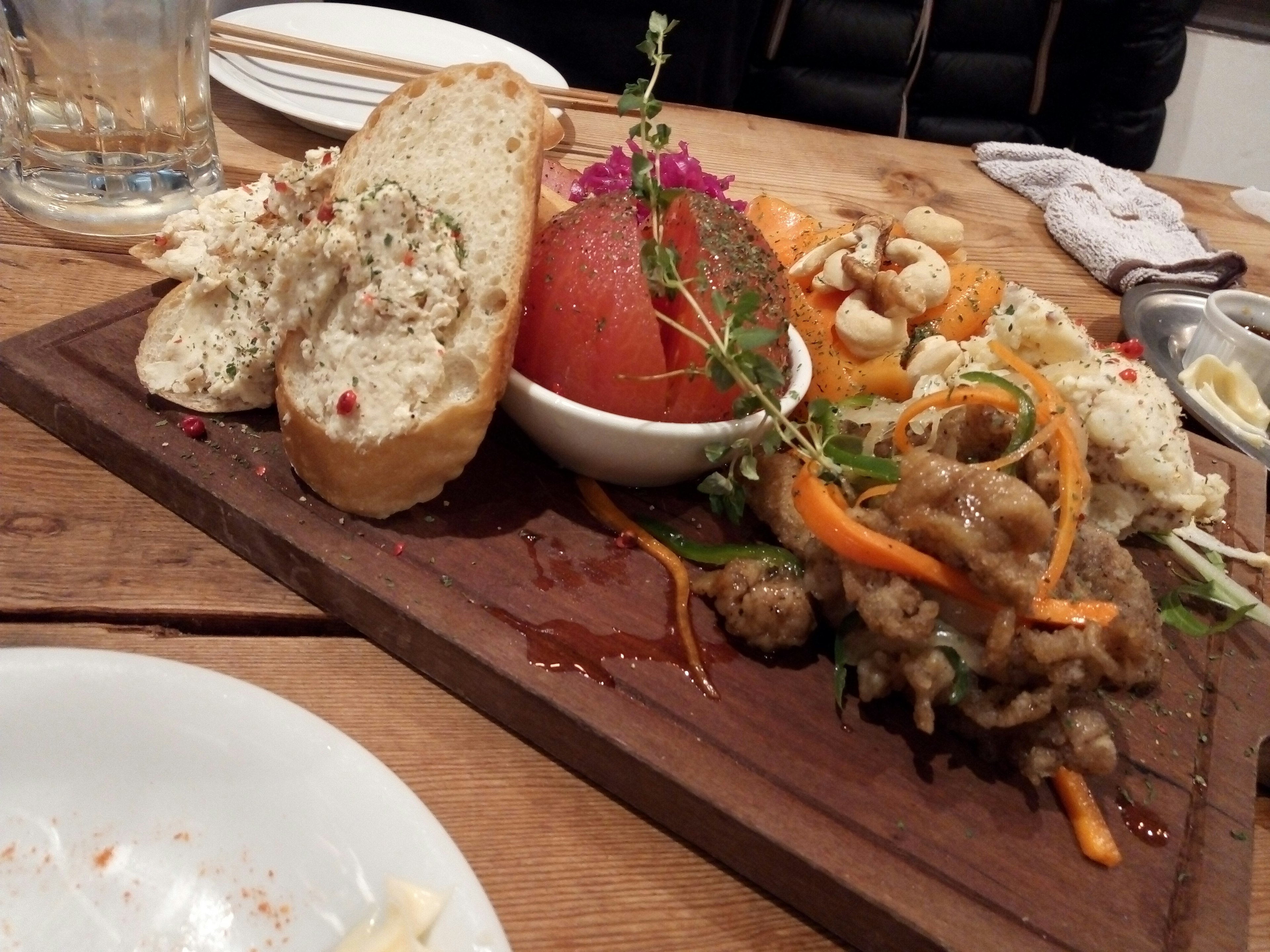 Plato de aperitivos dispuesto en una tabla de madera con verduras frescas y salsas