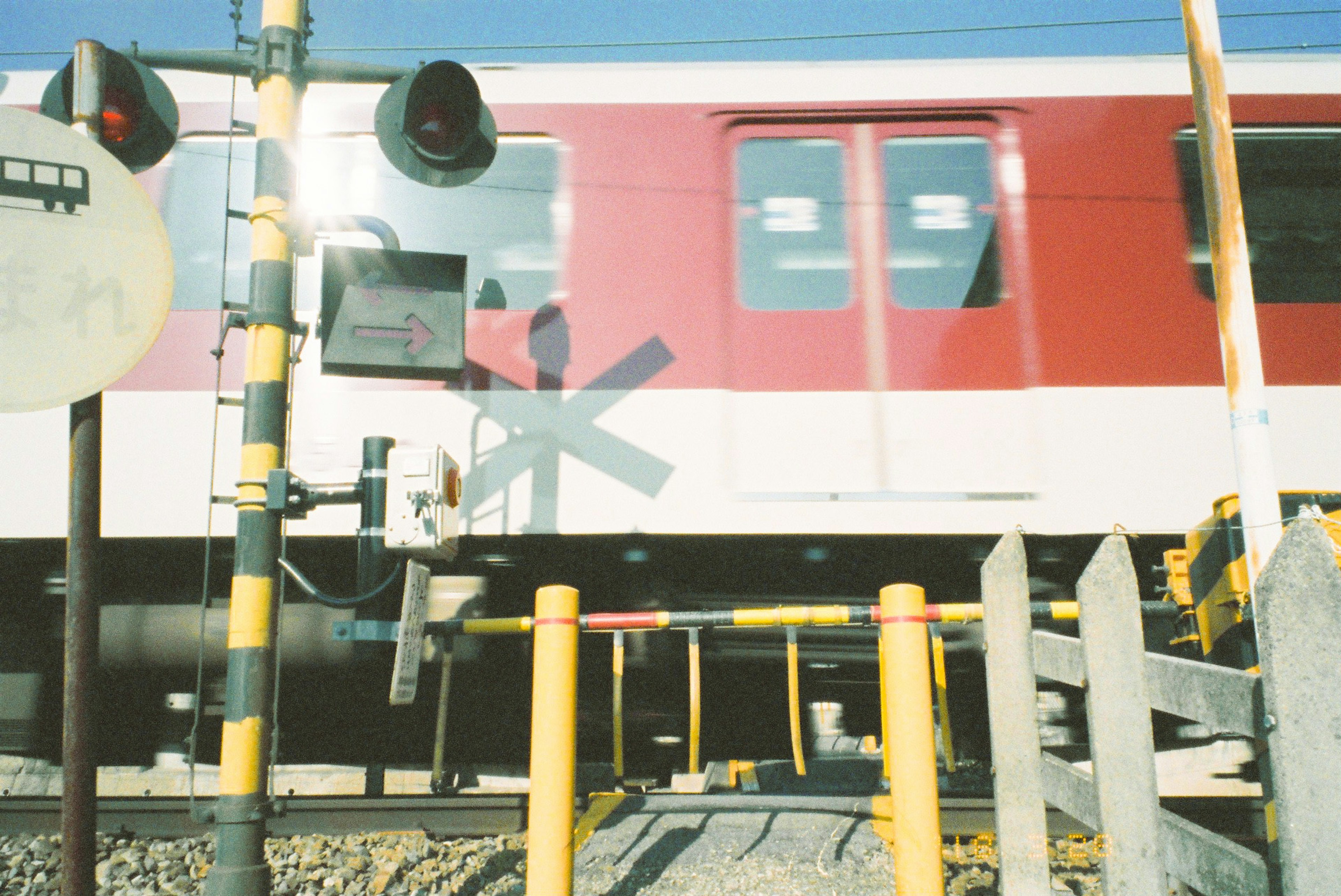 赤い電車が通過中で警告信号が点灯している踏切の風景