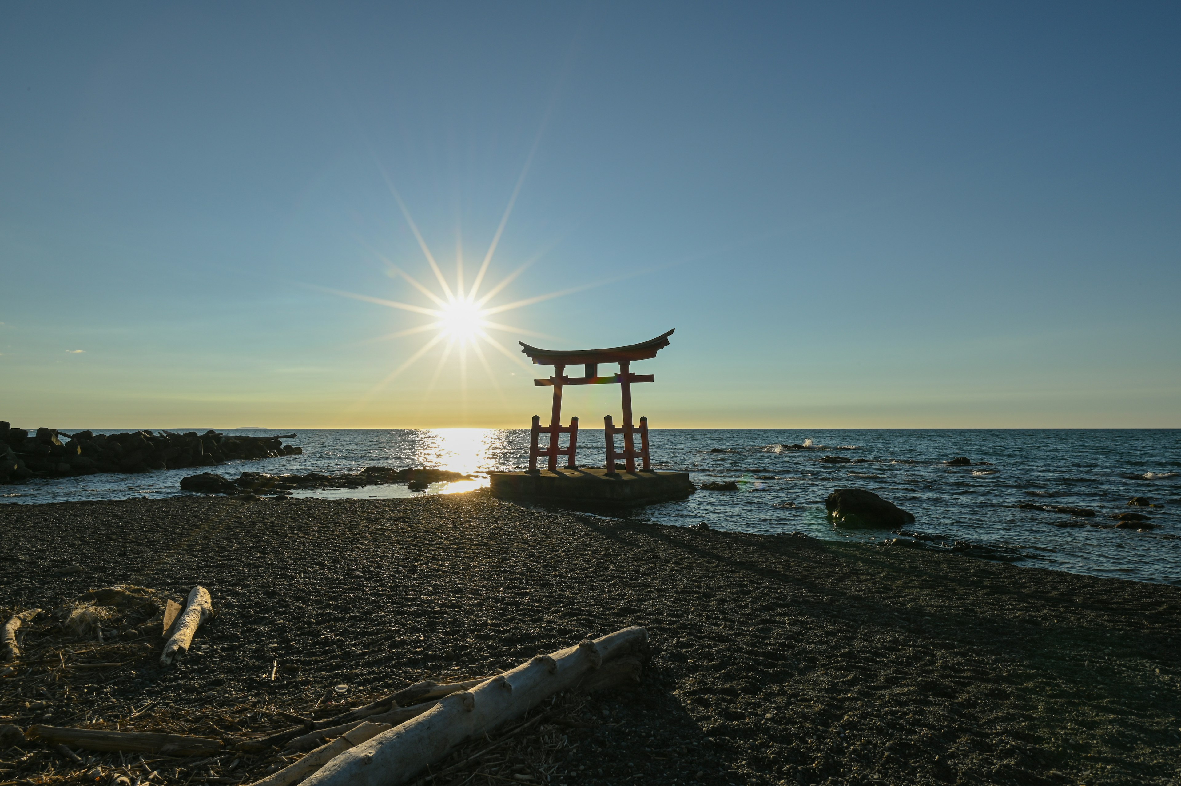 Torii-Tor am Strand mit Sonnenuntergang im Hintergrund