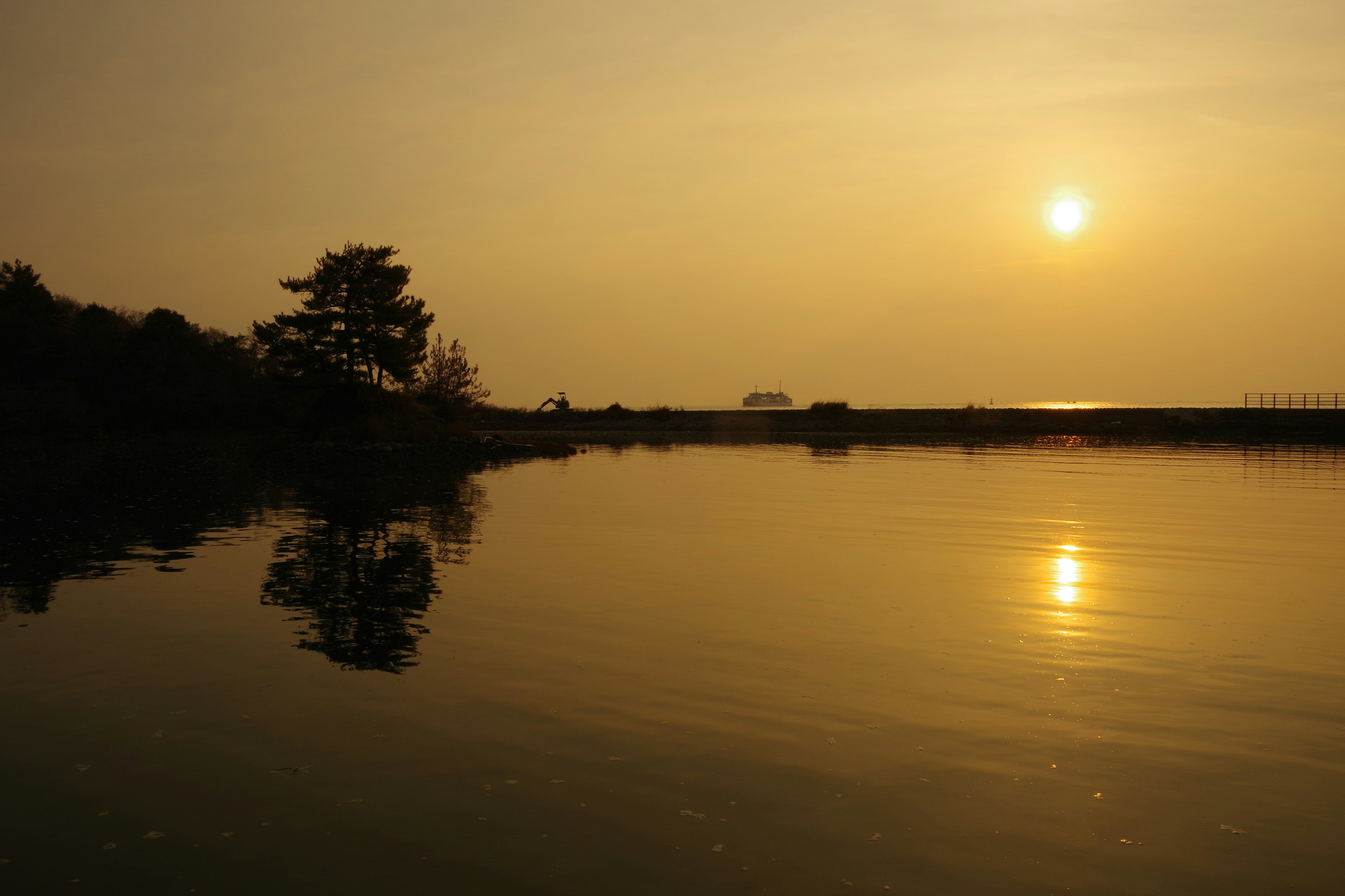 Paisaje sereno de lago al atardecer con reflejo del sol y silueta de árbol