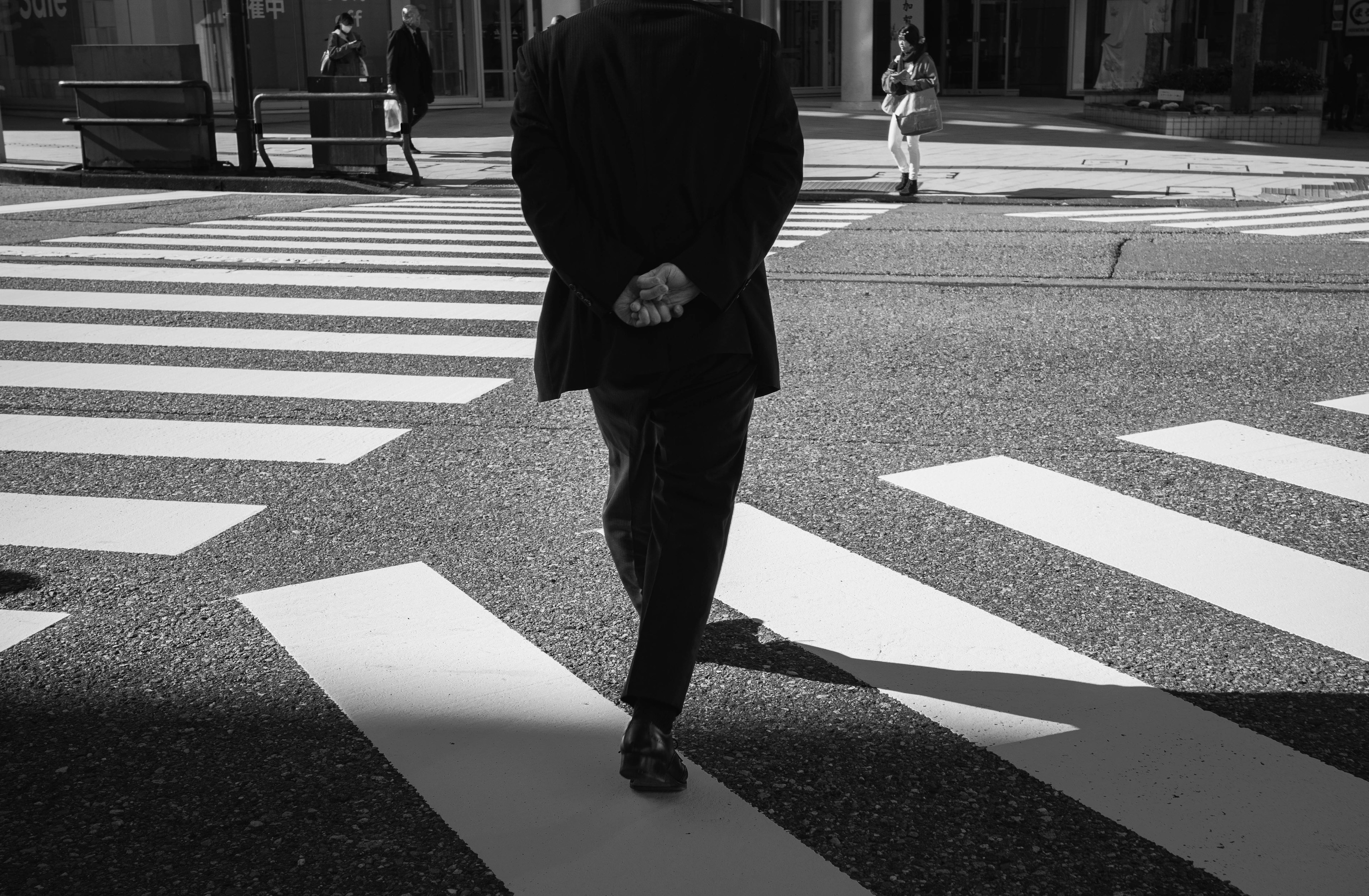 A man walking away in a black suit on a crosswalk