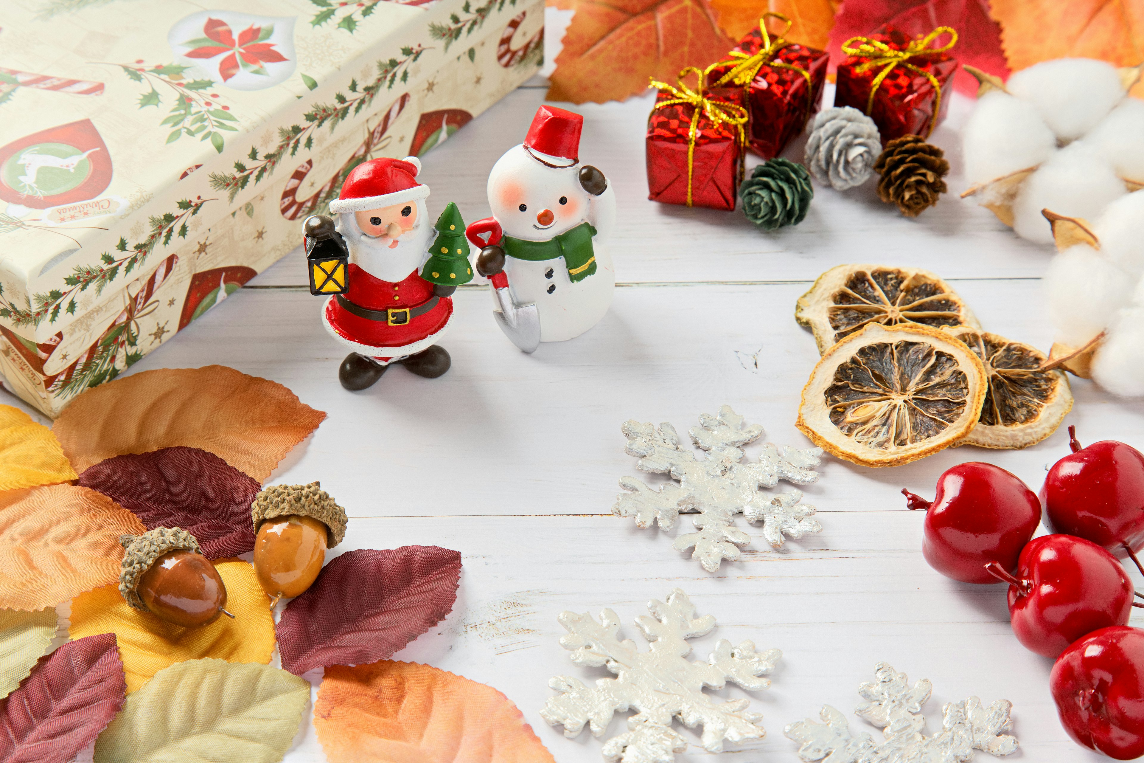 Scena decorativa con figurine di Babbo Natale e pupazzo di neve foglie autunnali arance essiccate e regali di Natale