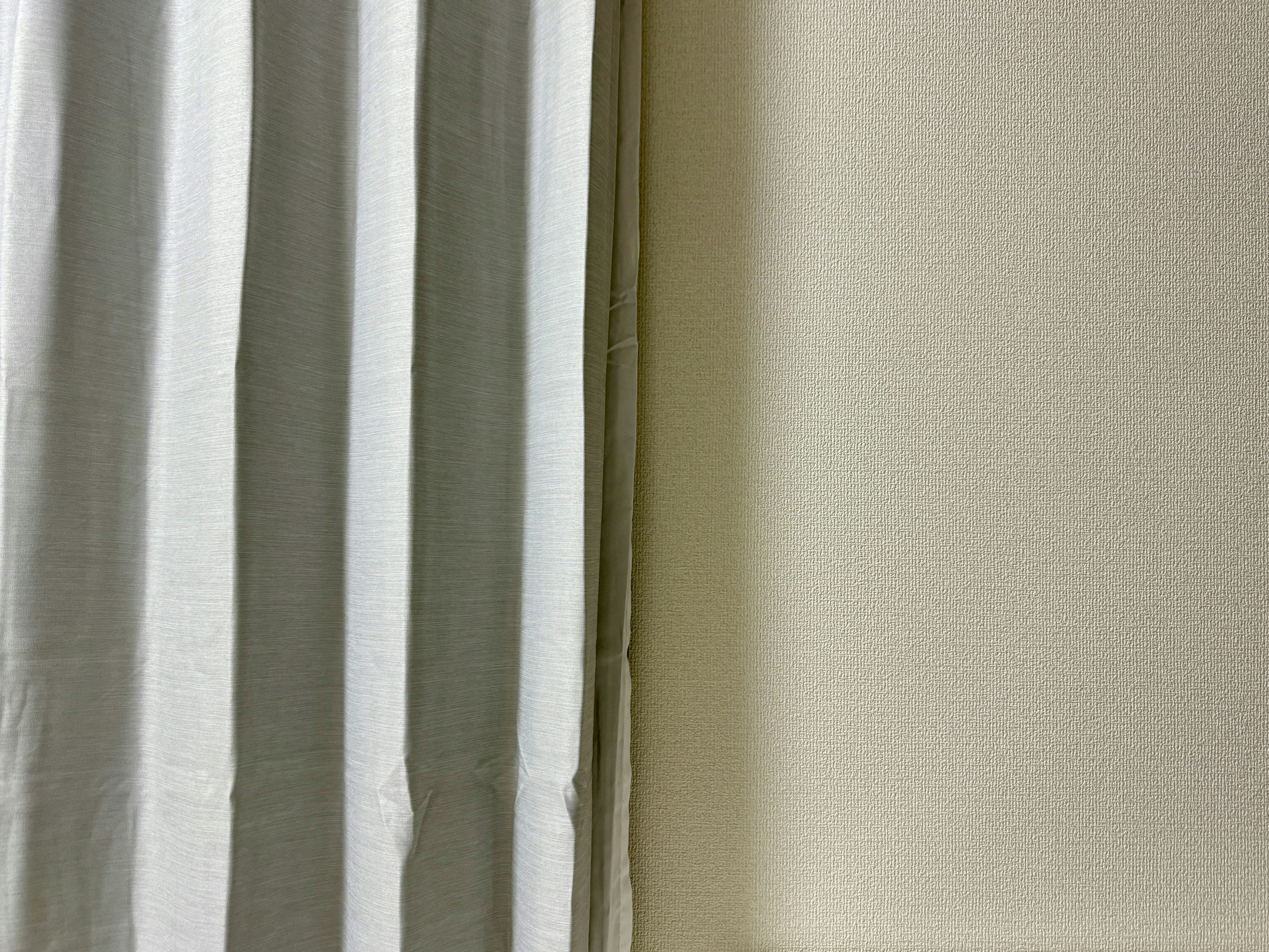 A corner of a room featuring white curtains and a light-colored wall