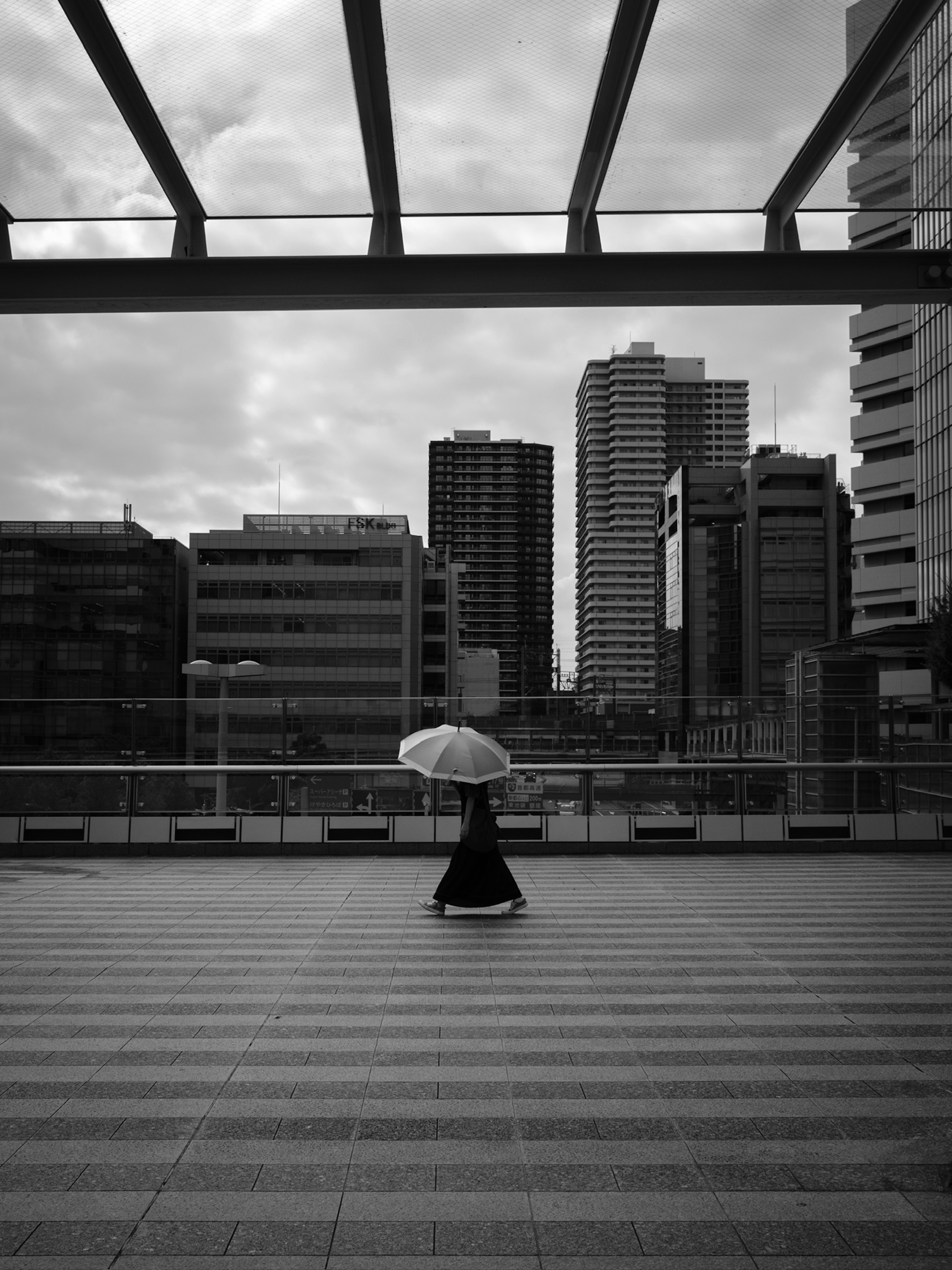 Mujer en kimono sosteniendo un paraguas frente a un paisaje urbano en blanco y negro