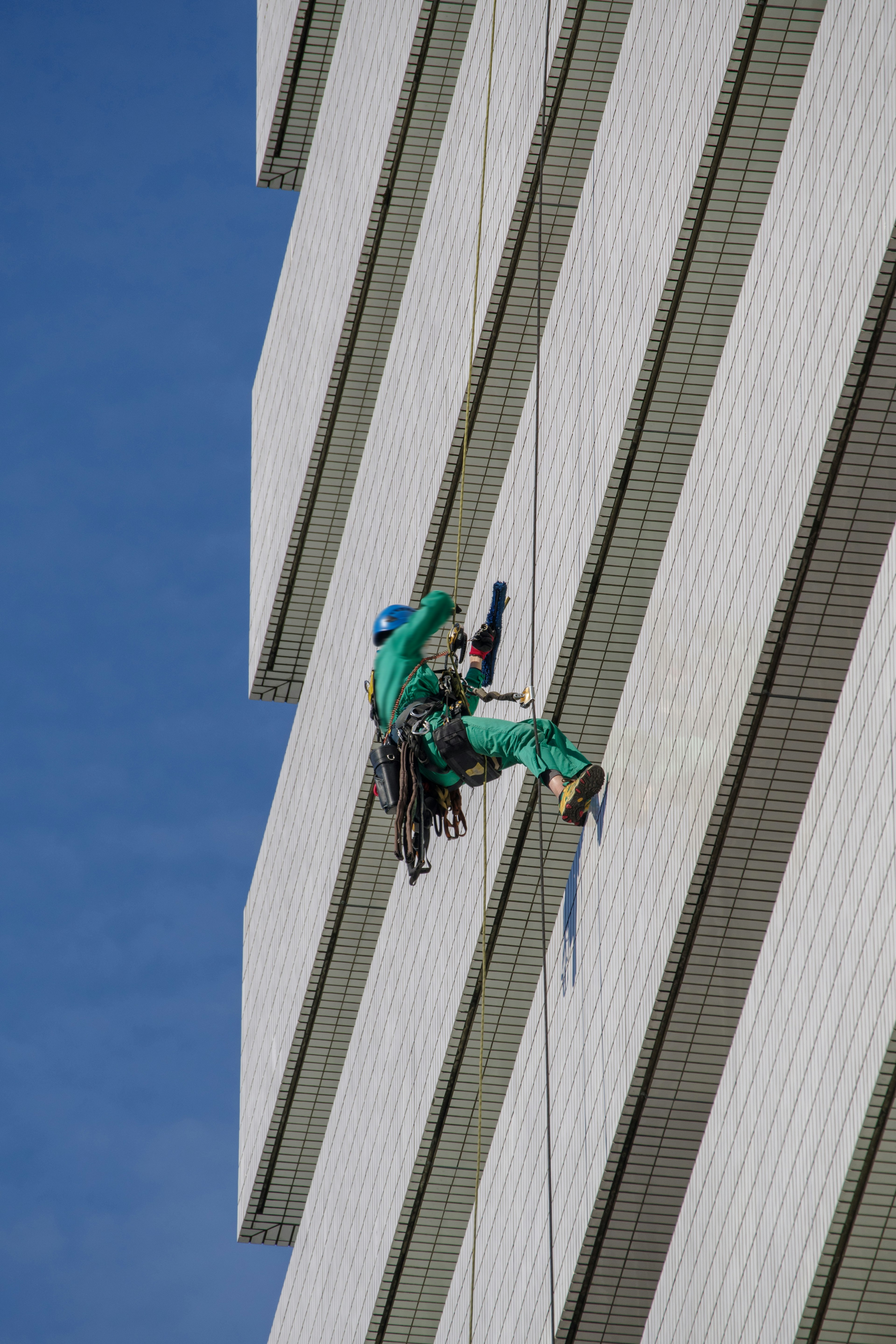 Trabajador con uniforme verde limpiando la fachada del edificio