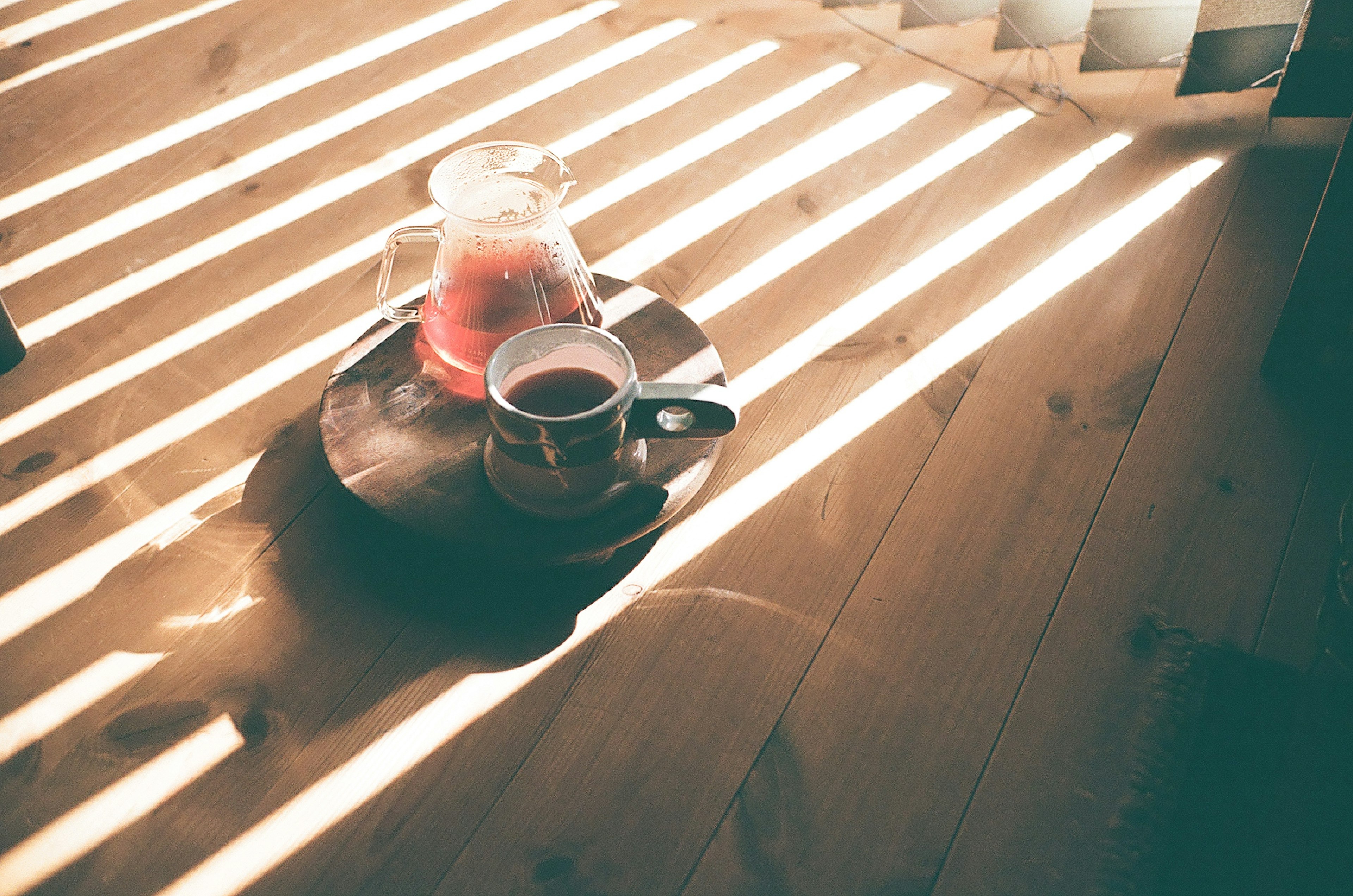 Cangkir kopi dan poci di atas meja dengan garis cahaya yang jatuh di lantai kayu