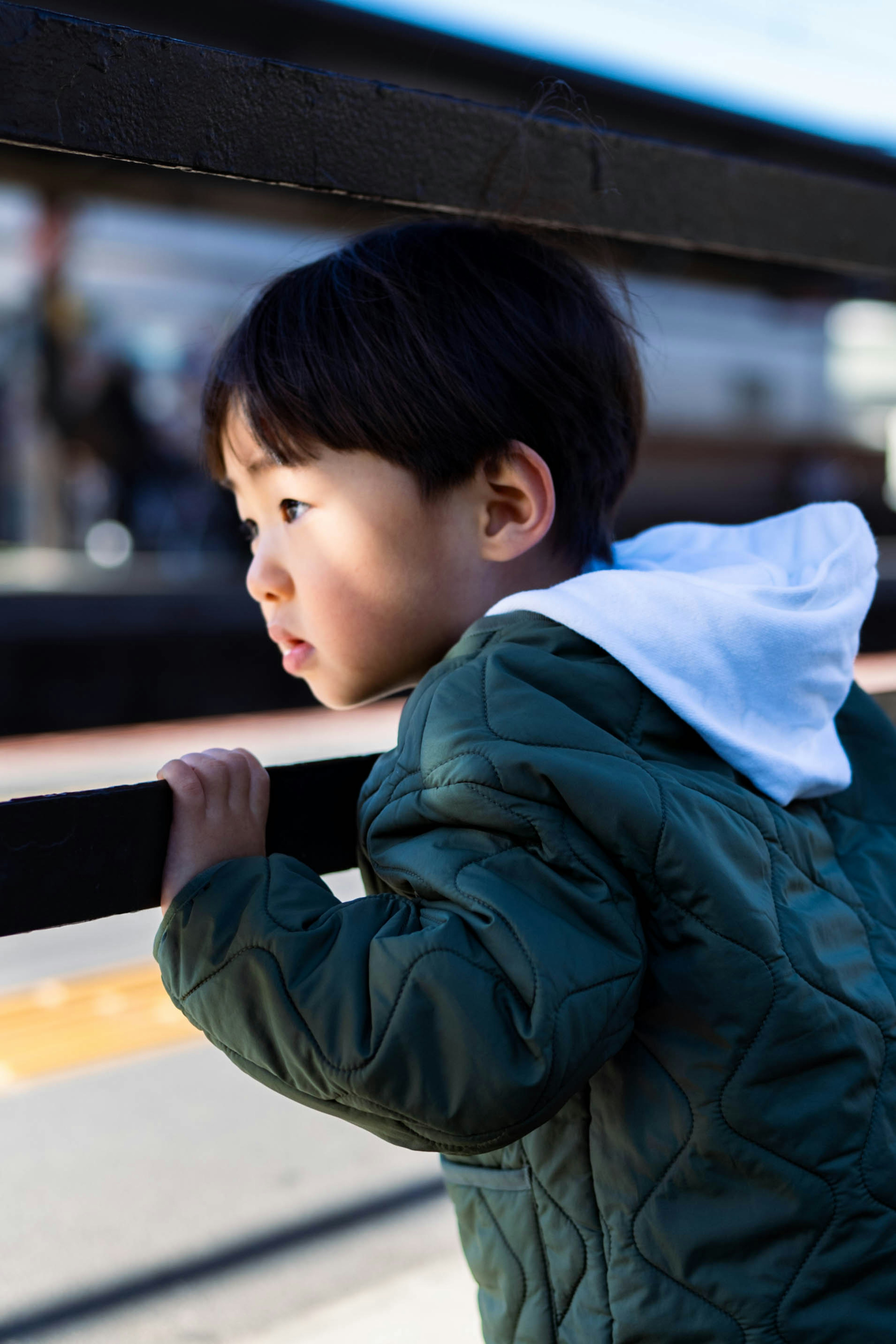 Un bambino appoggiato a una barriera con un'espressione pensierosa sfondo mostra una stazione ferroviaria e persone