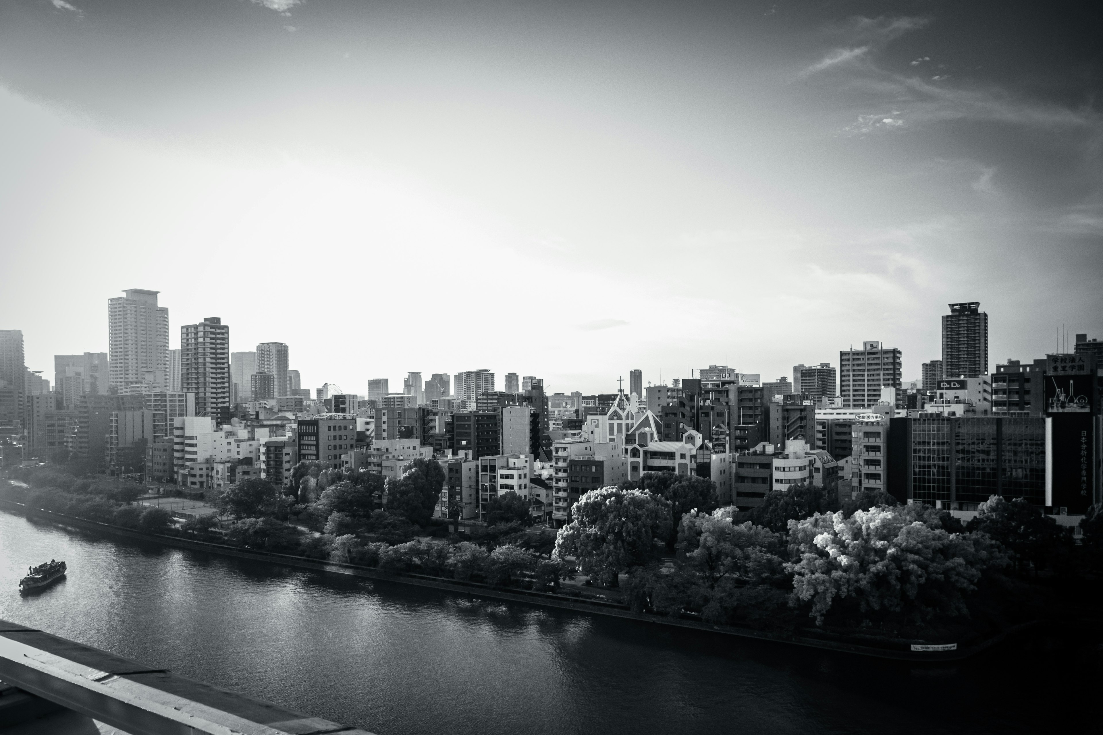 Black and white cityscape with a river featuring tall buildings and green trees