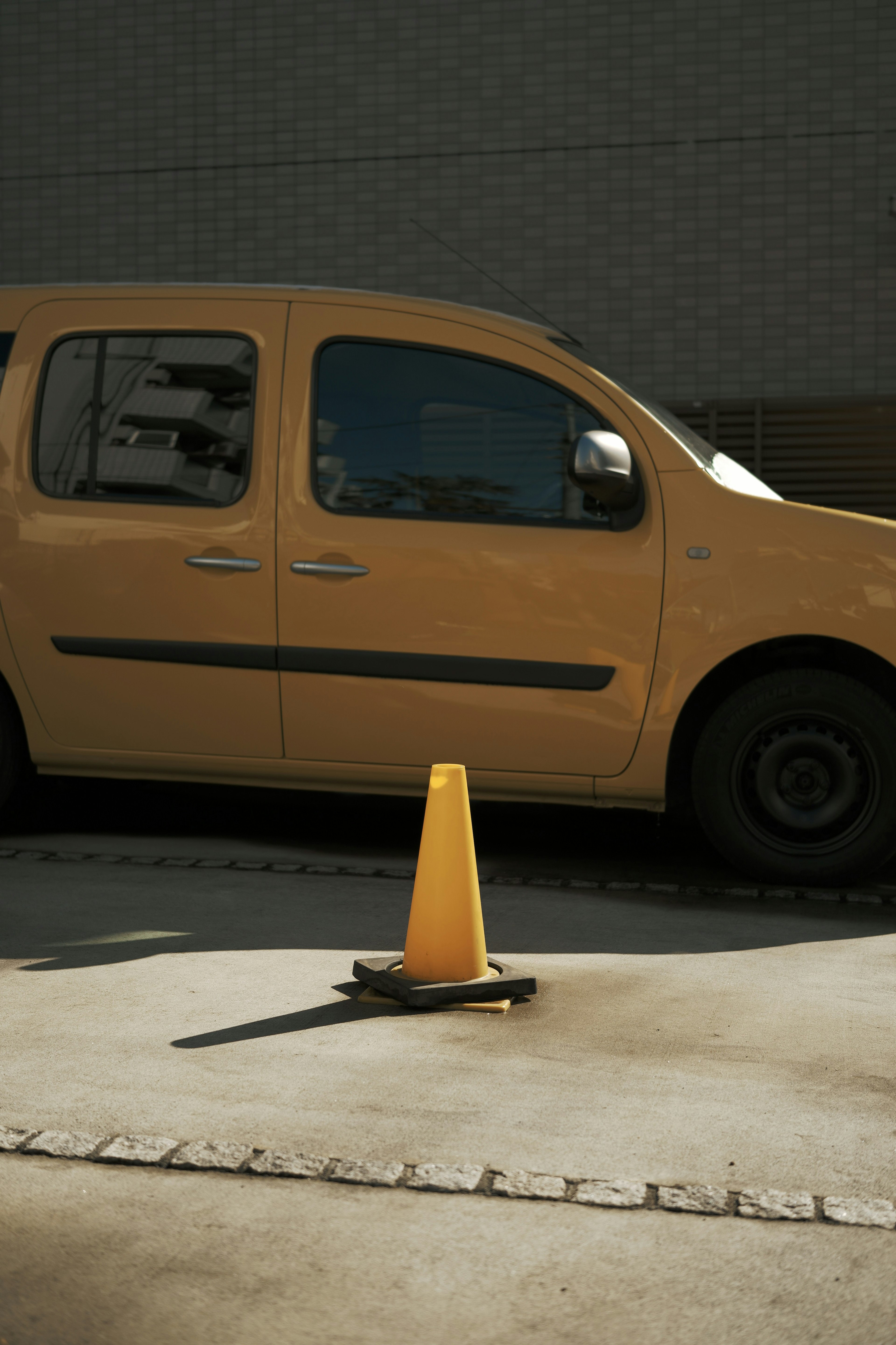 A yellow vehicle next to a traffic cone on the pavement