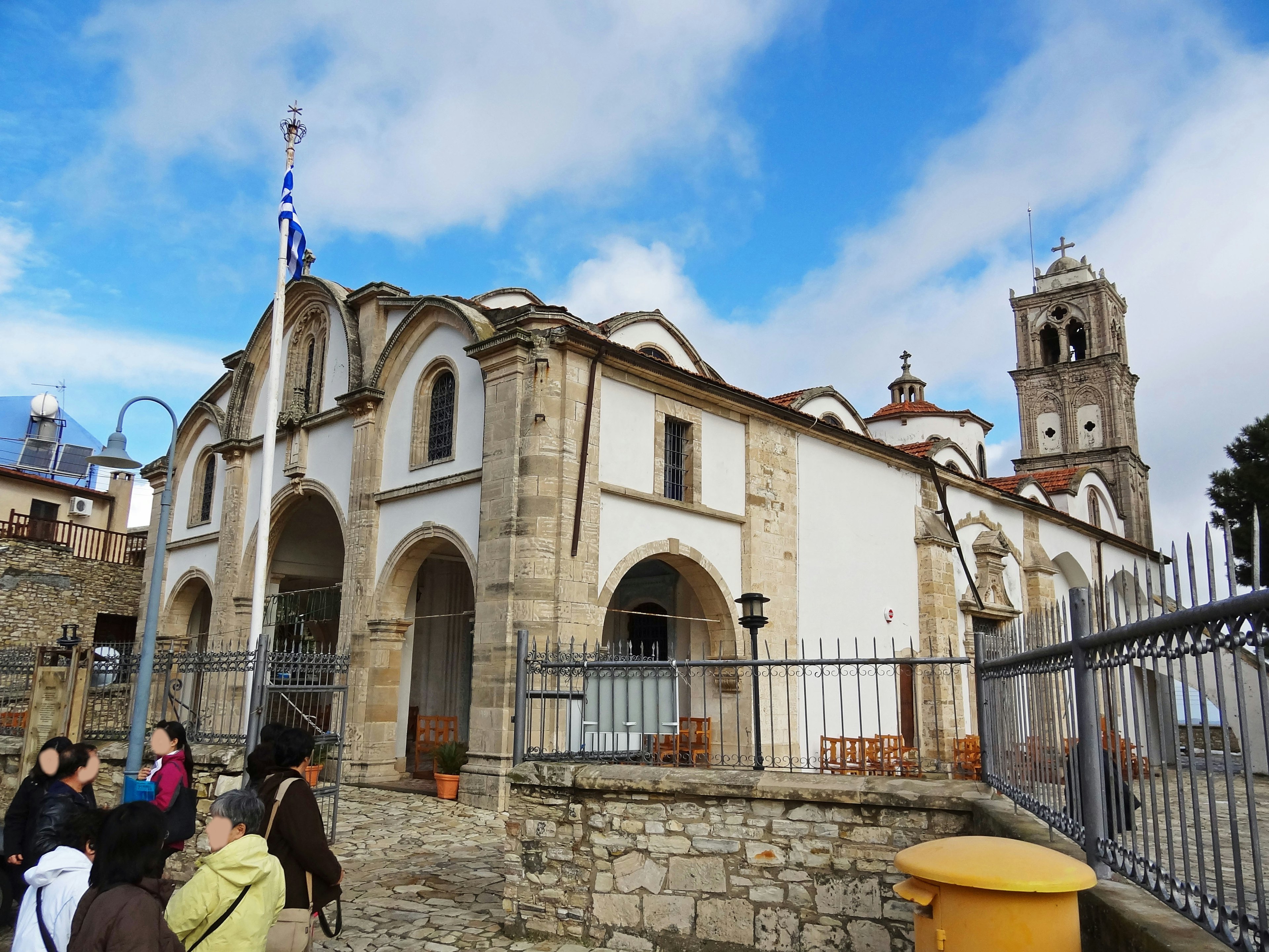 Iglesia histórica con arcos y una torre bajo un cielo azul con turistas