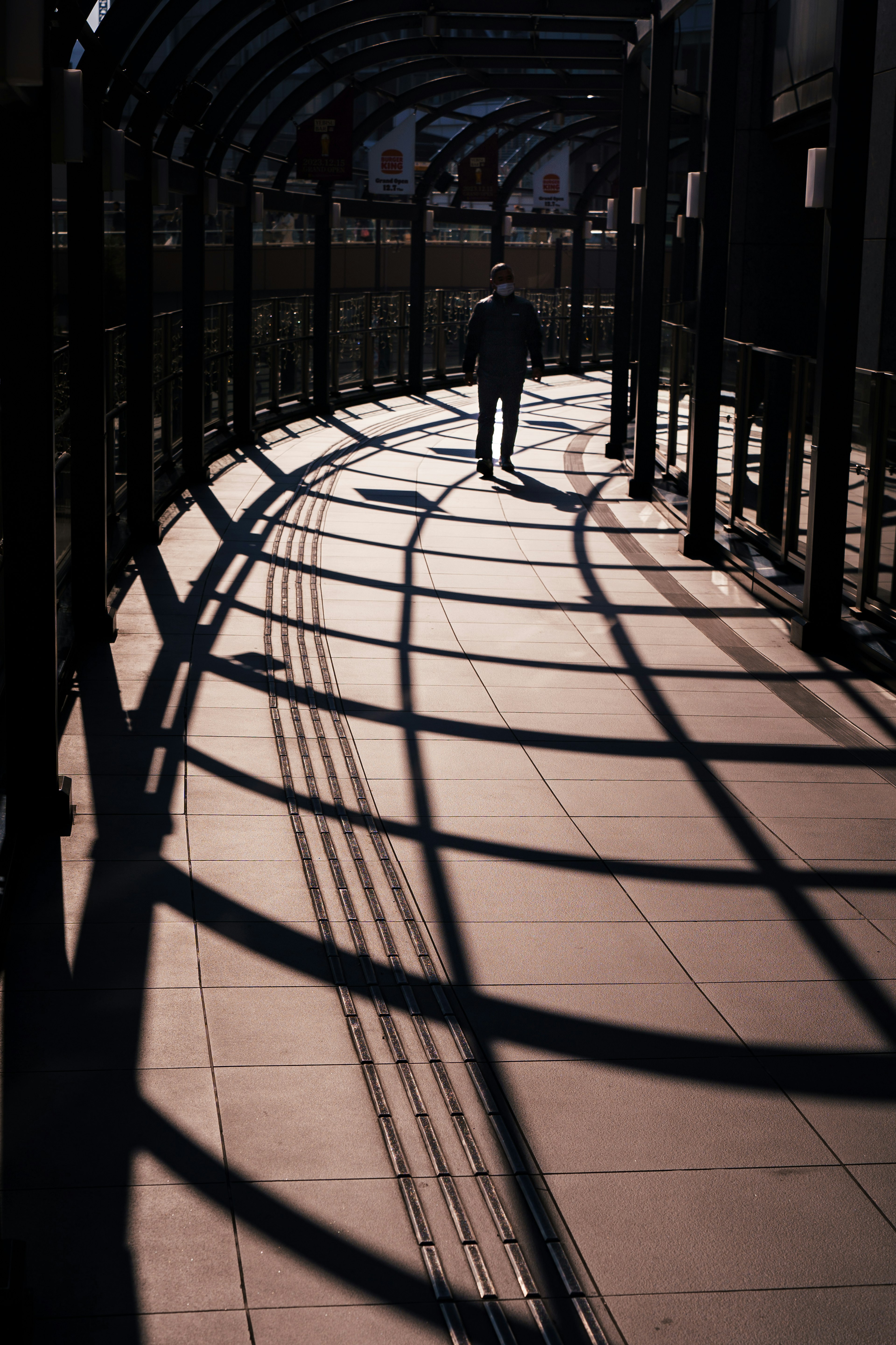 A person walking on a curved walkway with shadows cast by the structure