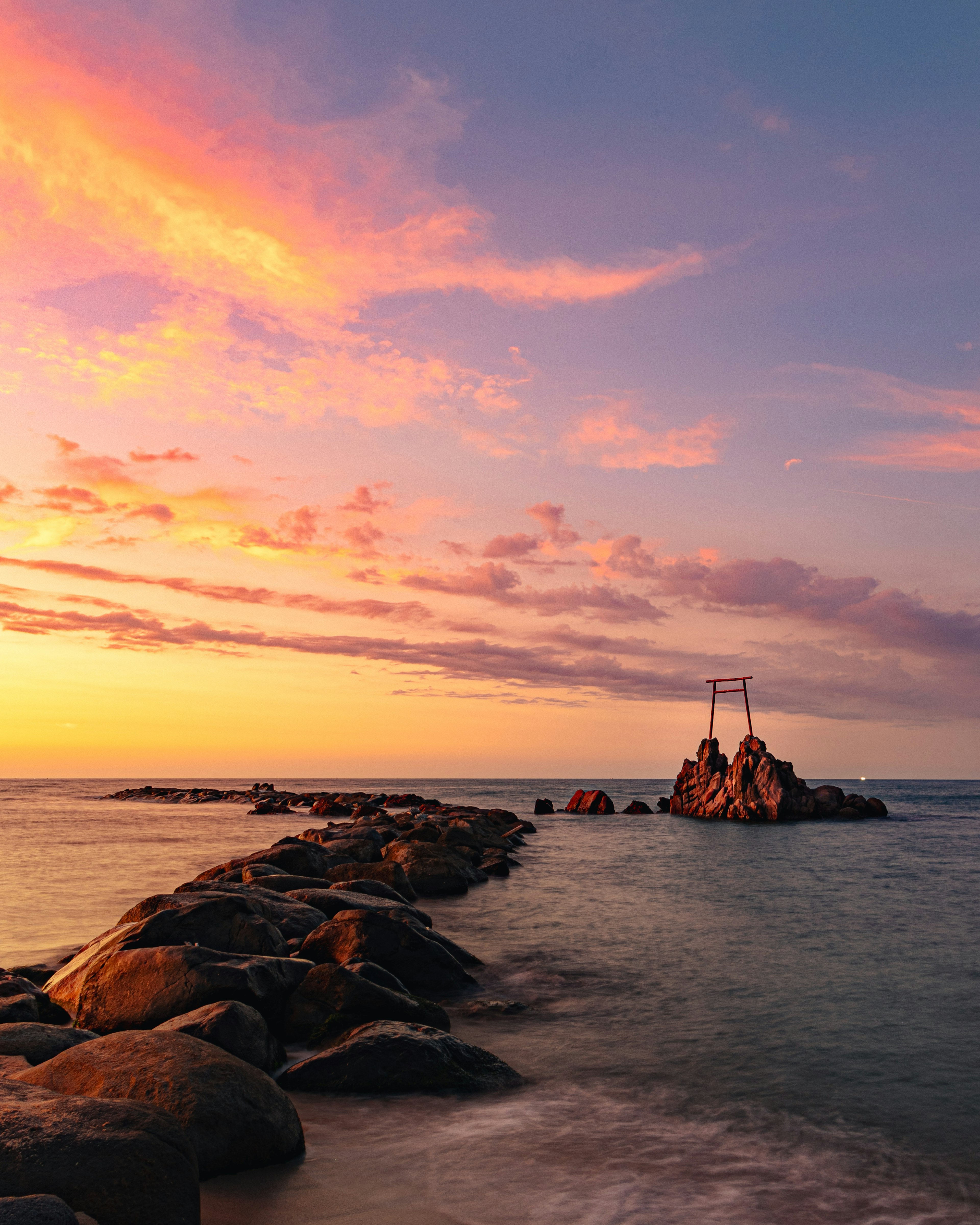 Jetée rocheuse au coucher du soleil avec ciel coloré et vagues calmes