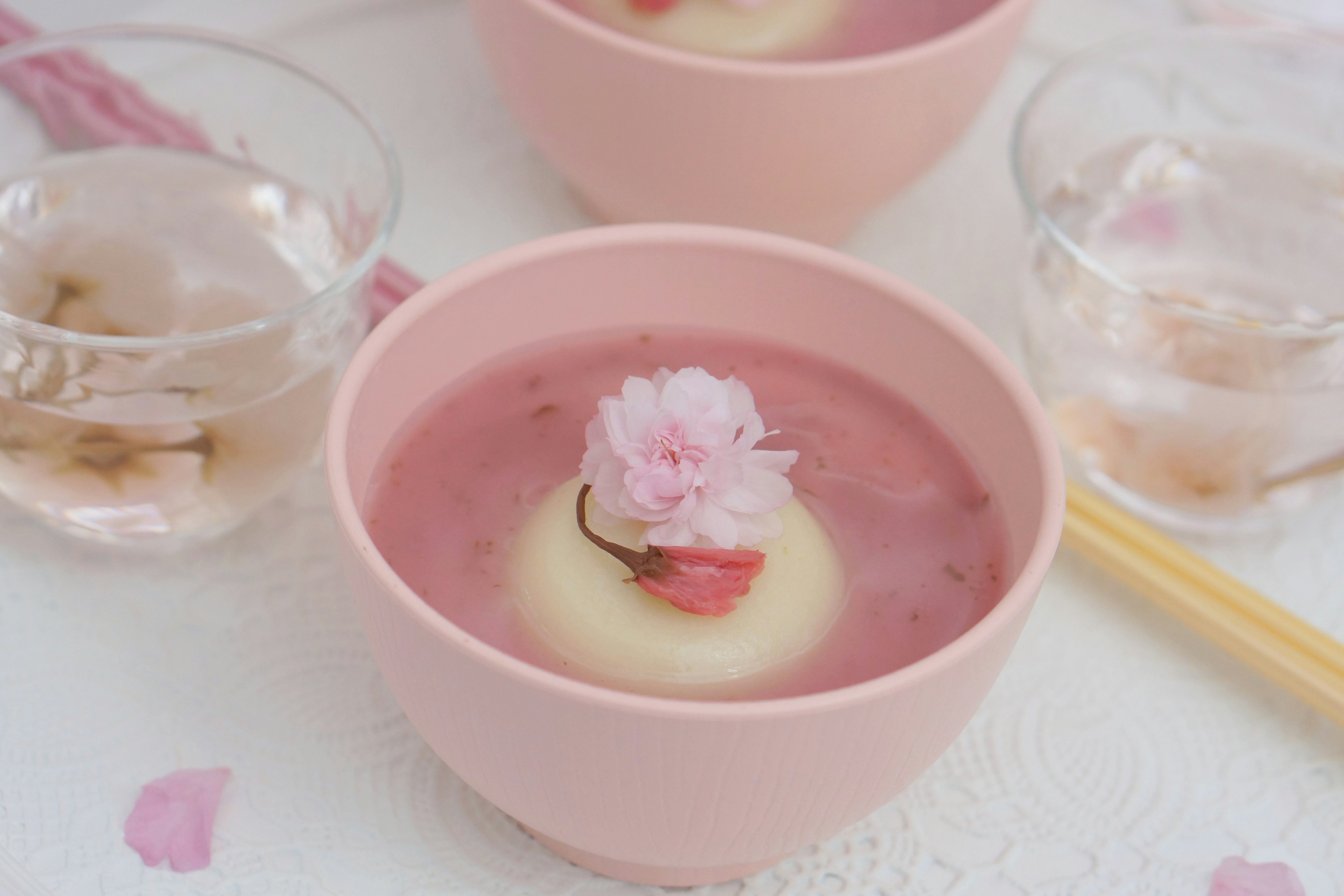 Une belle mise en place de table avec un dessert rose contenant une fleur de cerisier flottante et des verres transparents à côté