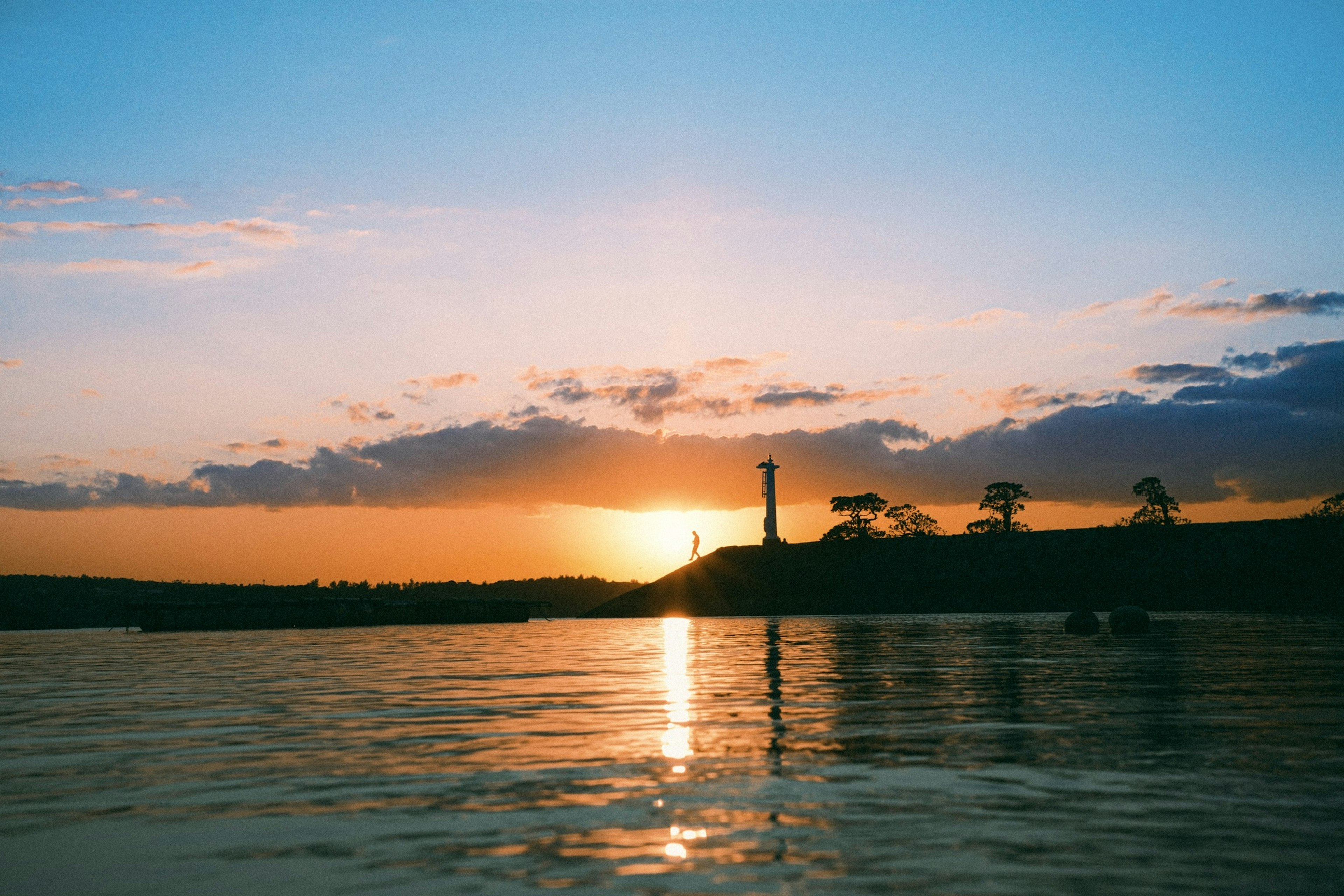 Malersicher Blick auf den Sonnenuntergang über Wasser mit der Silhouette eines Leuchtturms