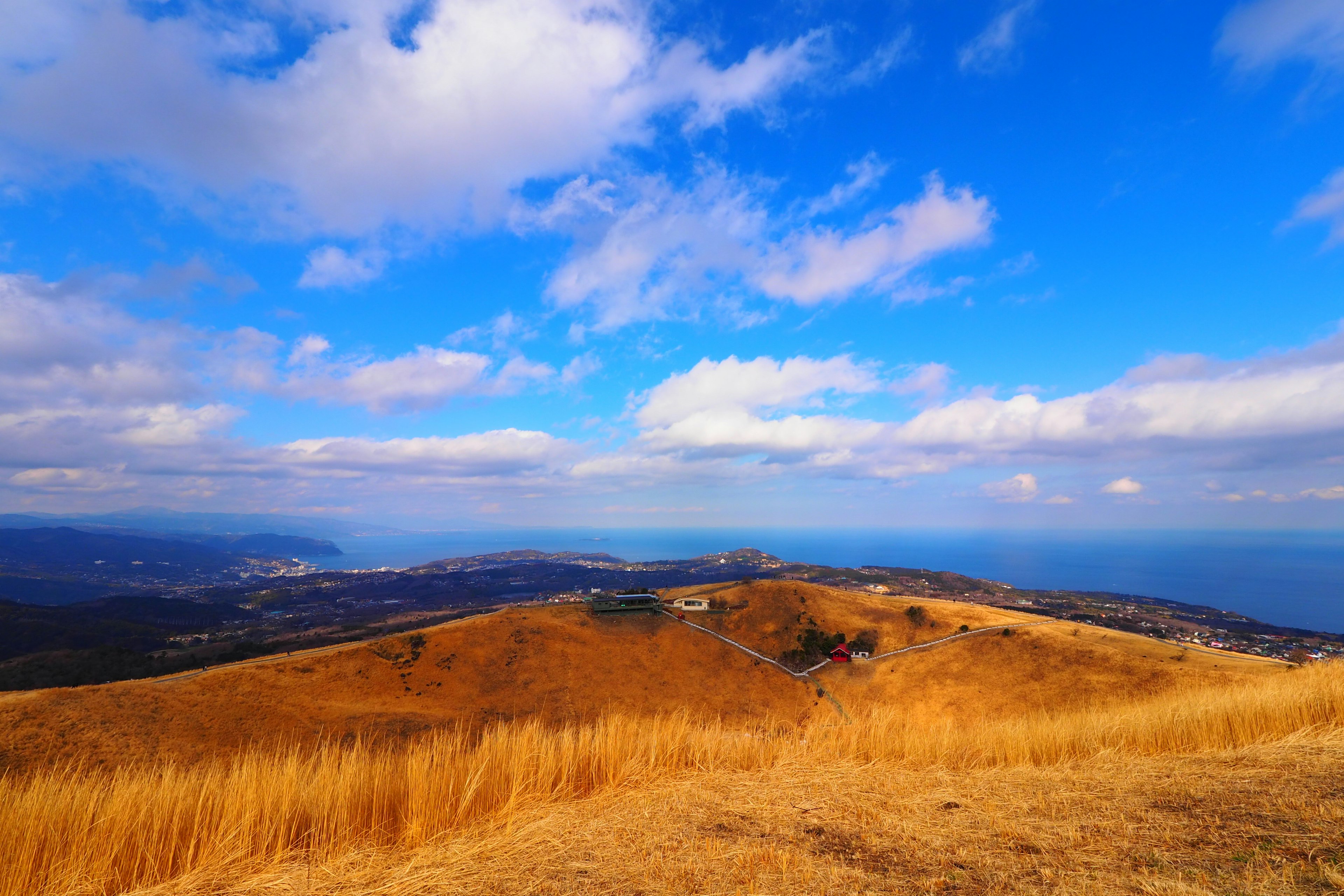 Colline secca sotto un cielo blu con nuvole sparse che sovrastano il mare