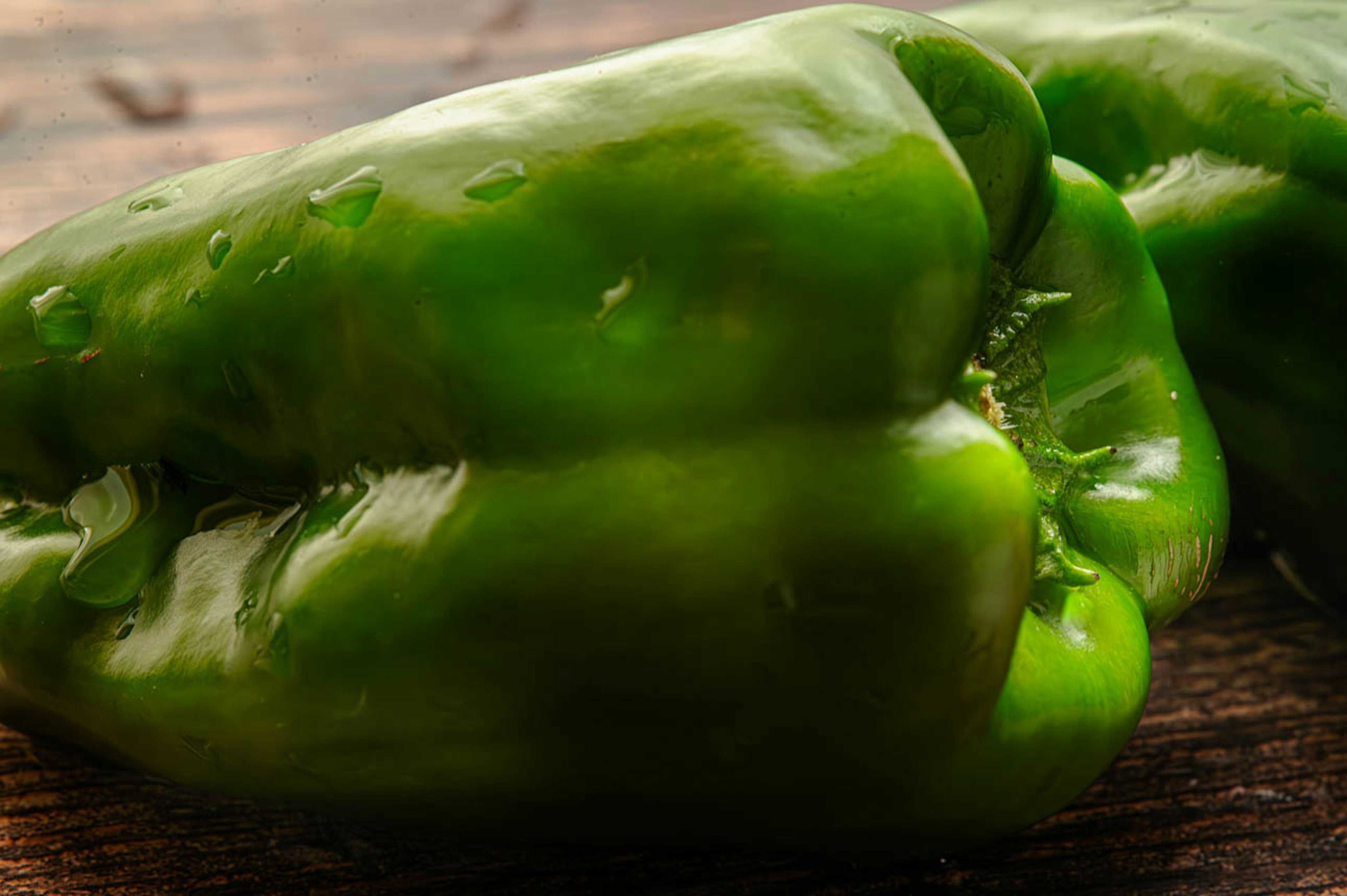 Fresh green bell peppers resting on a wooden surface