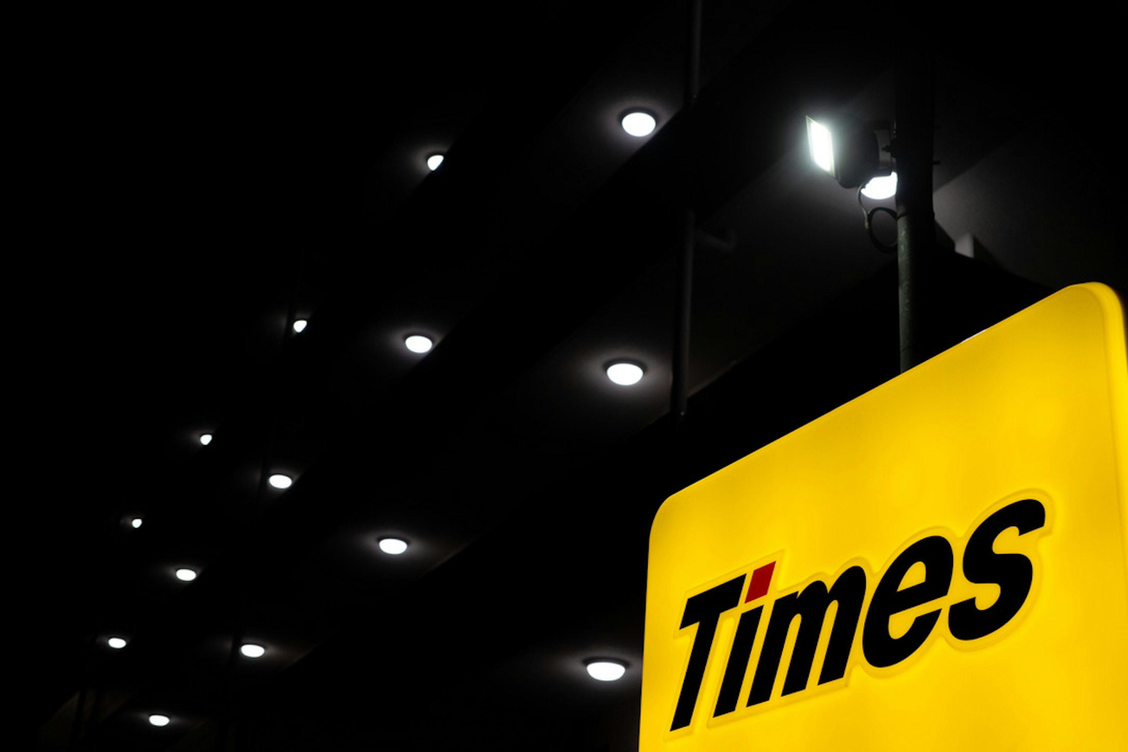 A bright yellow sign with black lettering reading 'Times' against a dark background with shining lights