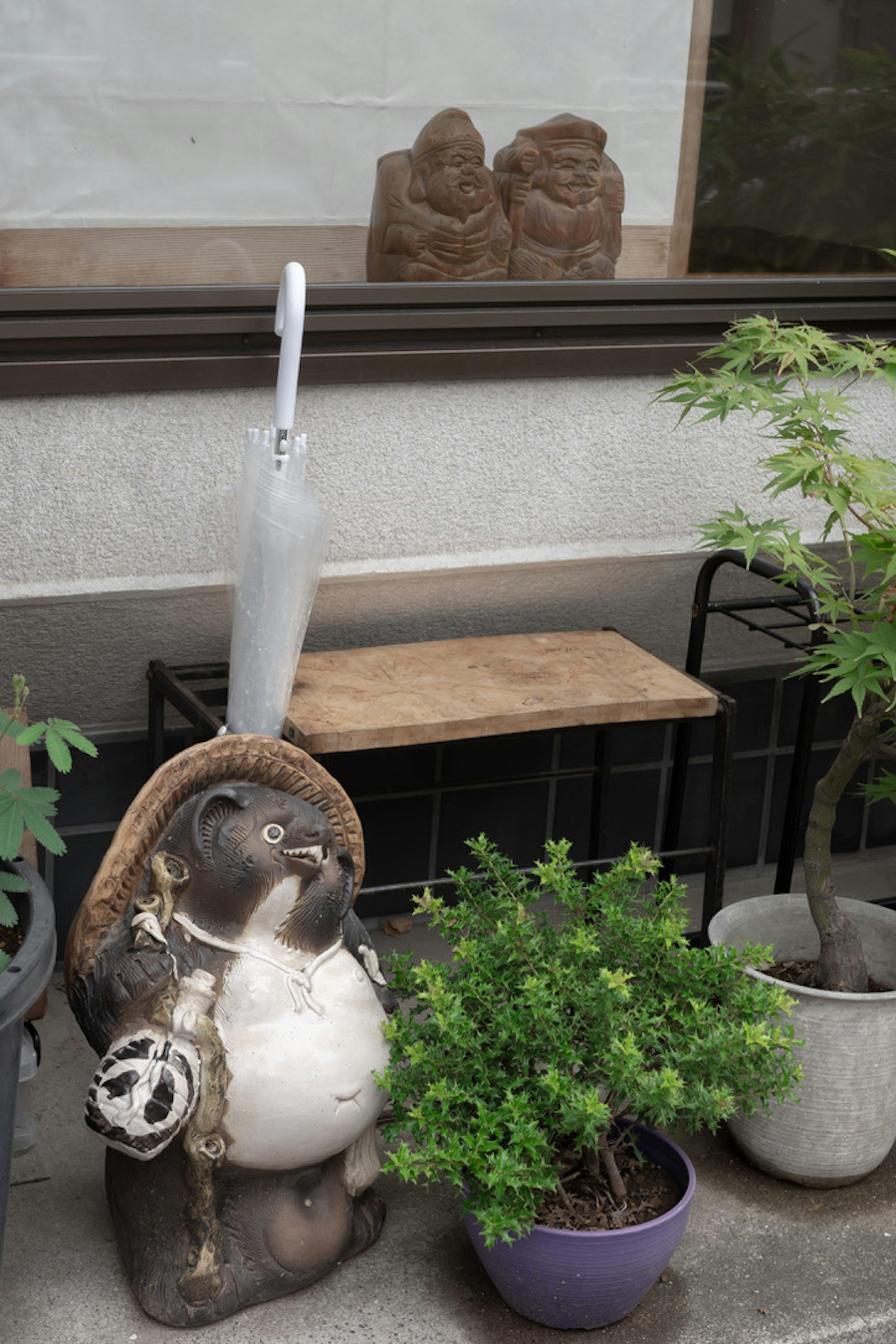 A tanuki statue holding an umbrella next to potted plants and a wooden bench