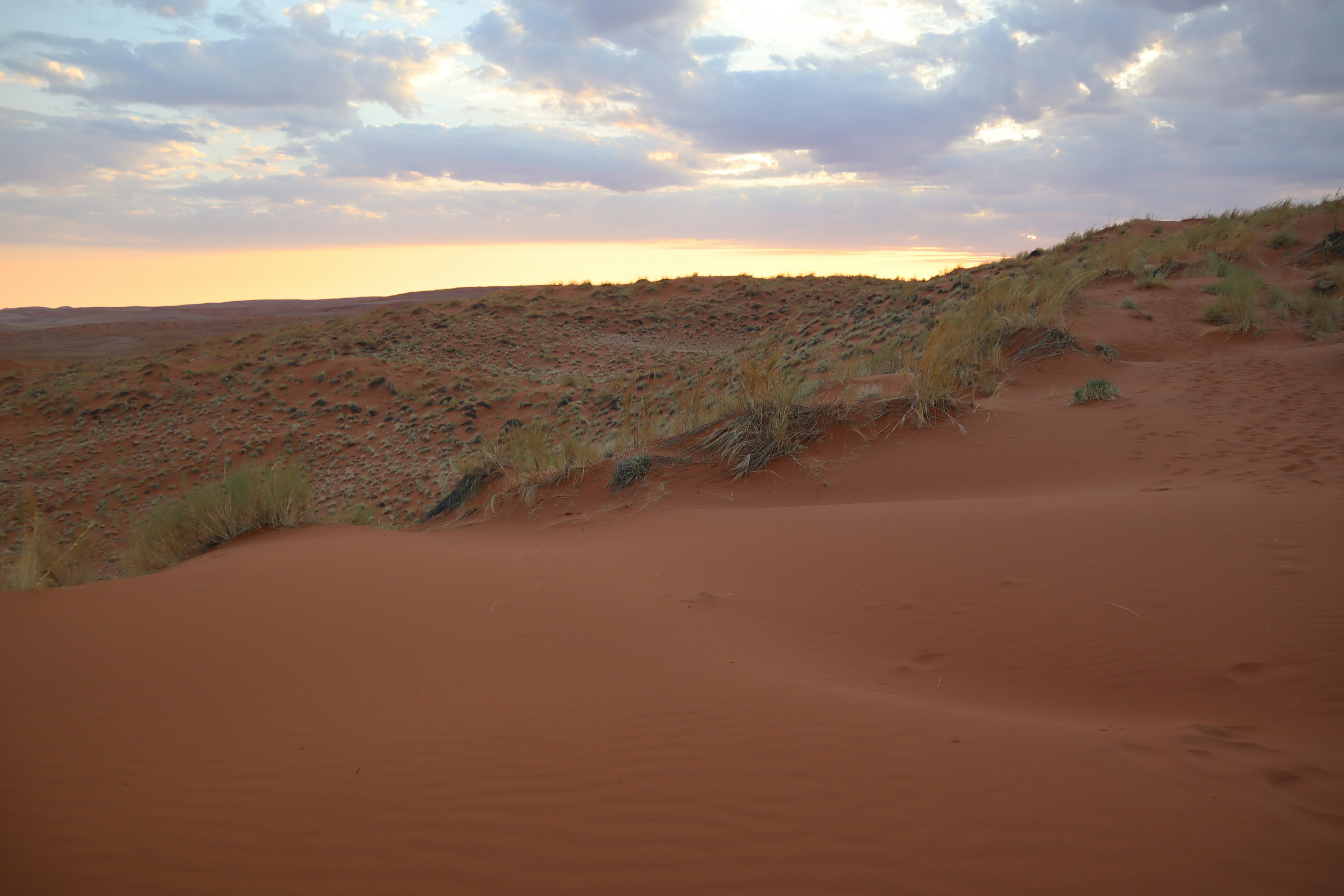 Dune di sabbia rossa che si estendono sotto un cielo nuvoloso sereno