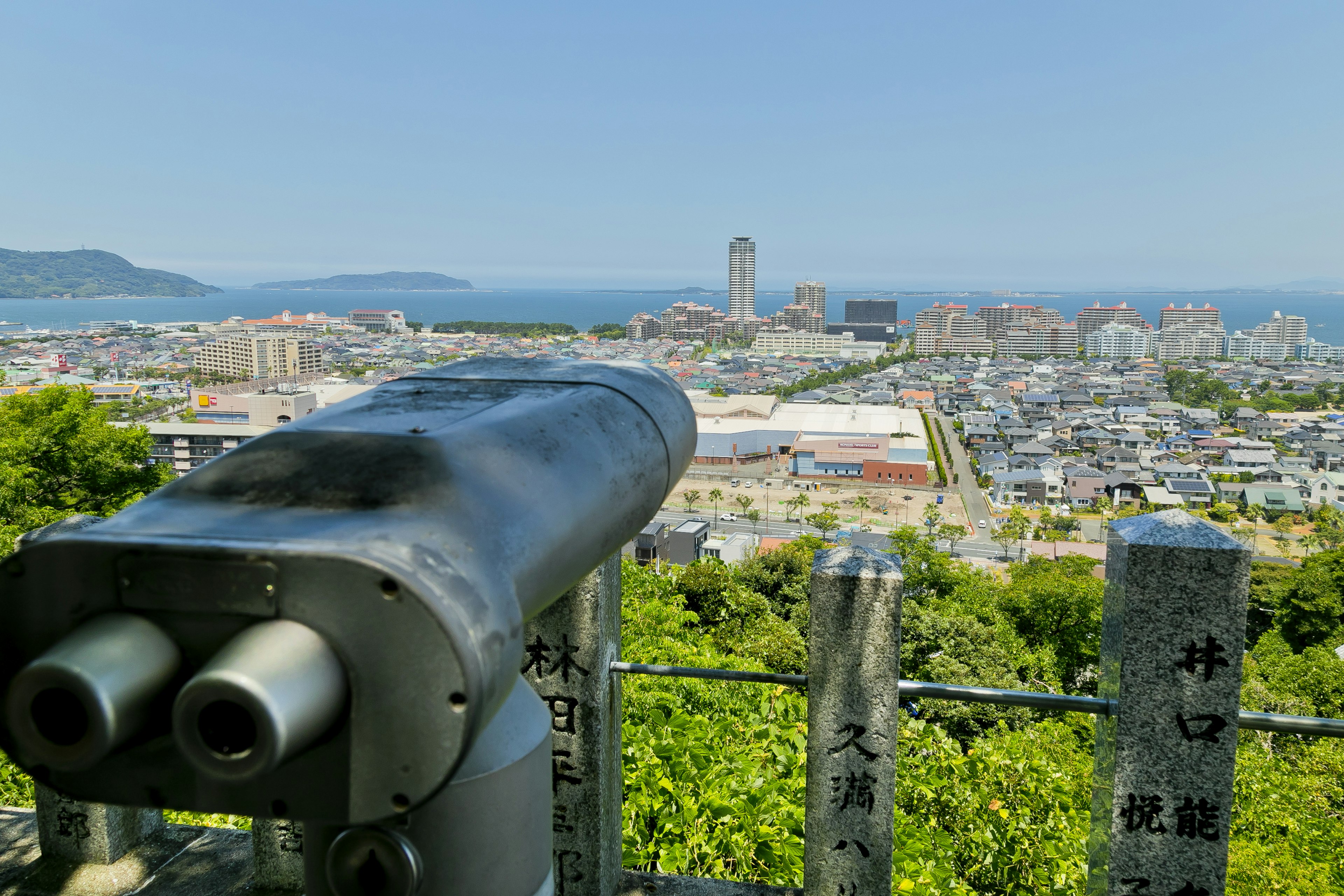 View from an observation deck featuring the sea and city skyline with a silver binocular in the foreground