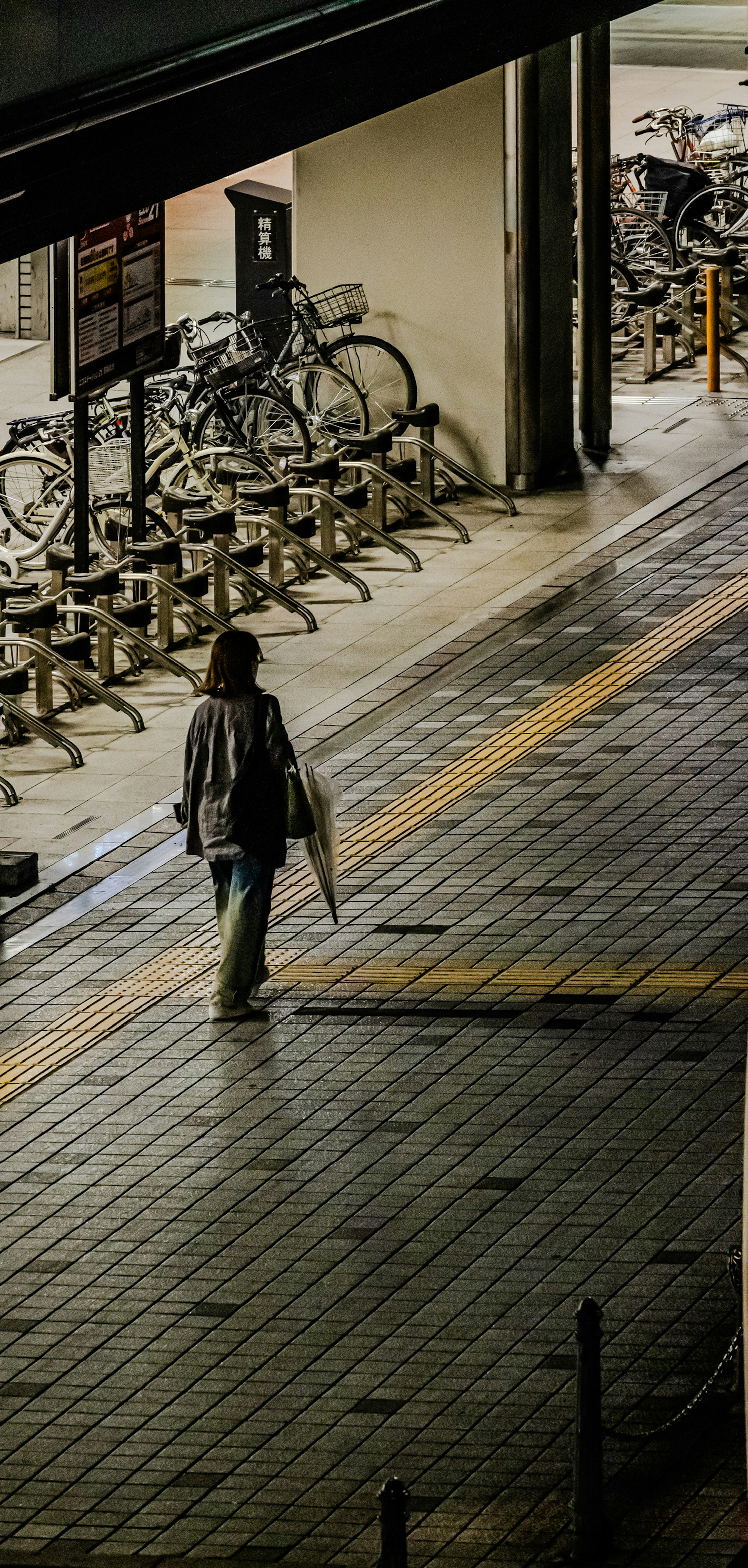 傘を持って歩く人と自転車ラックのある夜の街角