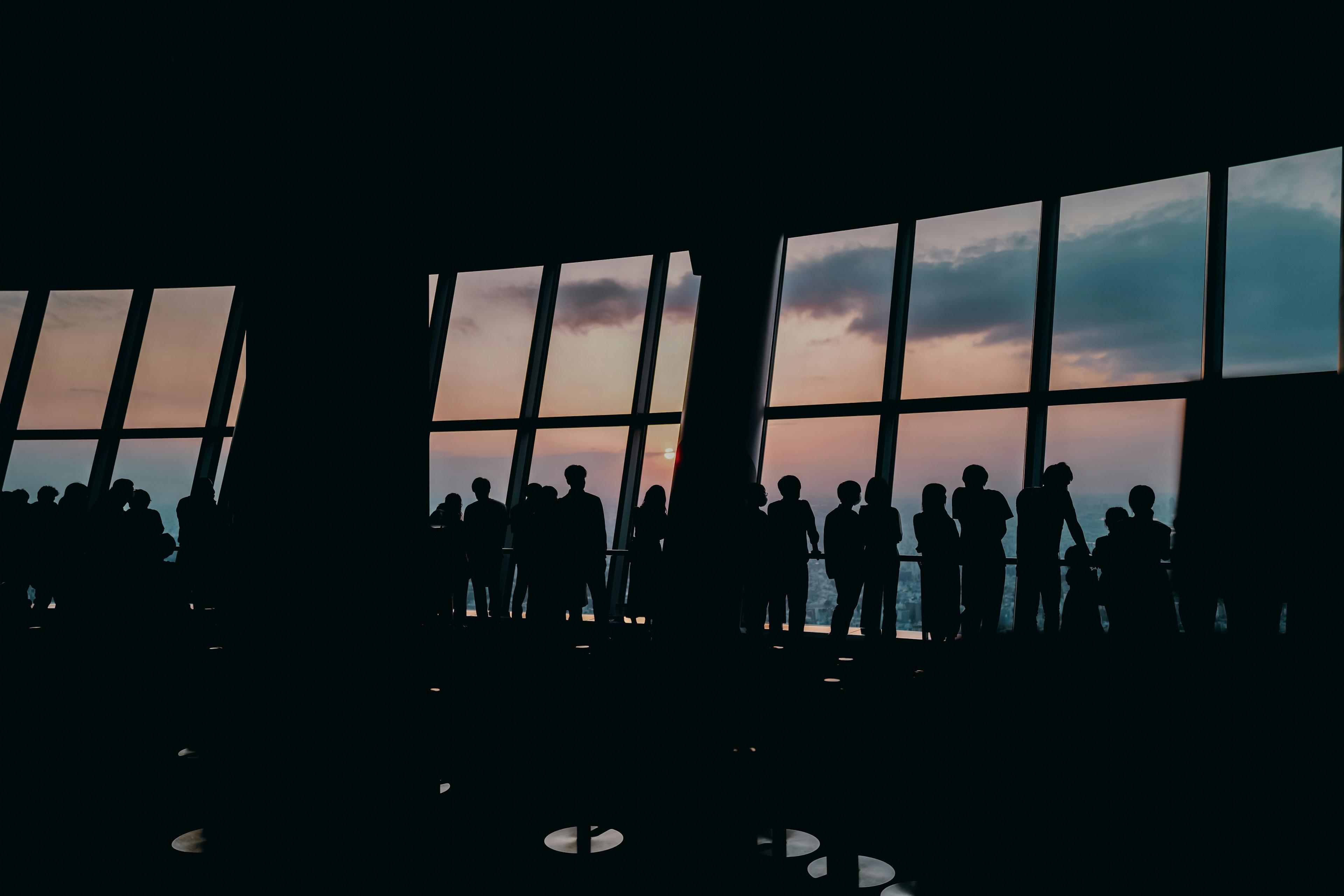 Silhouetten von Menschen vor einem Sonnenuntergang, gesehen durch große Fenster