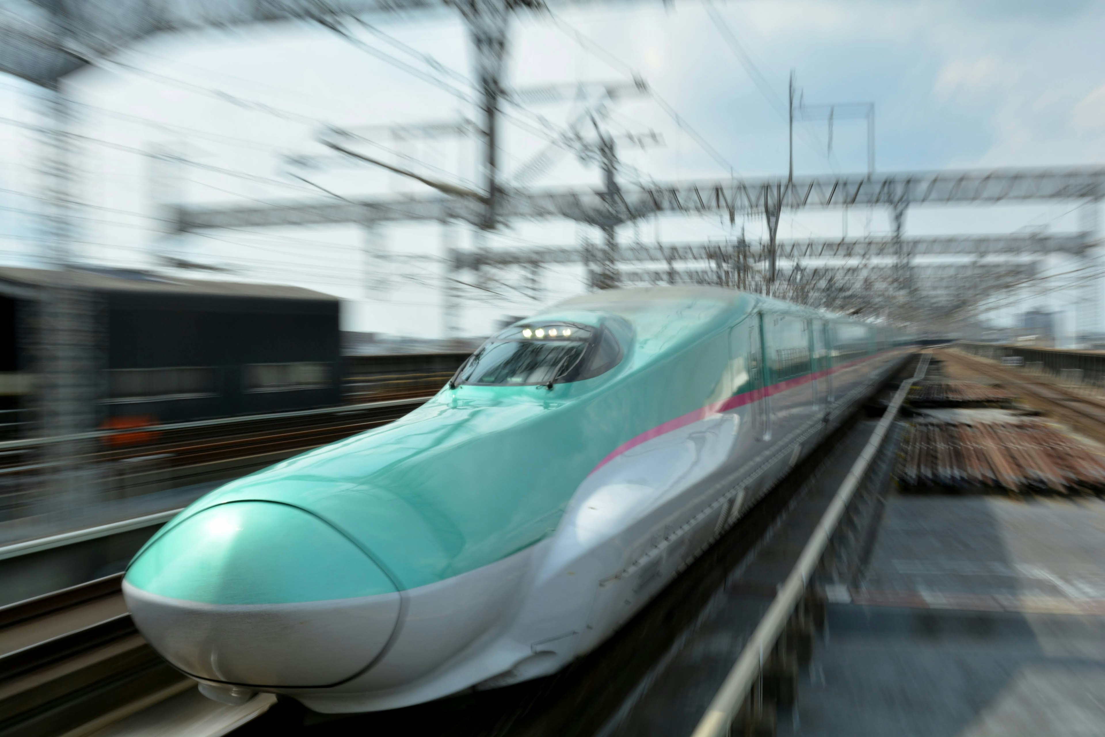 Shinkansen traveling at high speed with overhead railway lines in the background