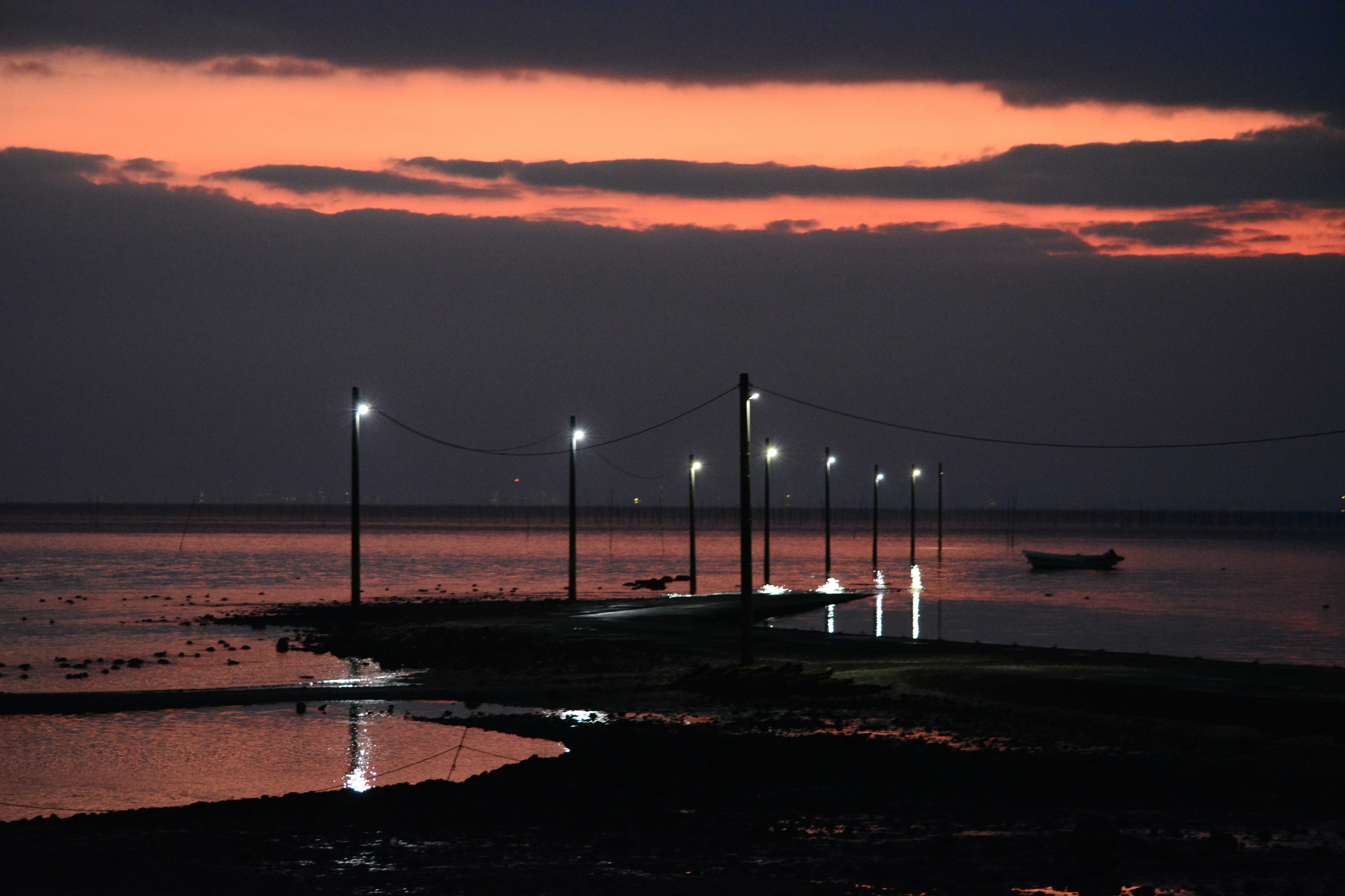 夕焼けの中に灯りが灯る桟橋と静かな海の風景