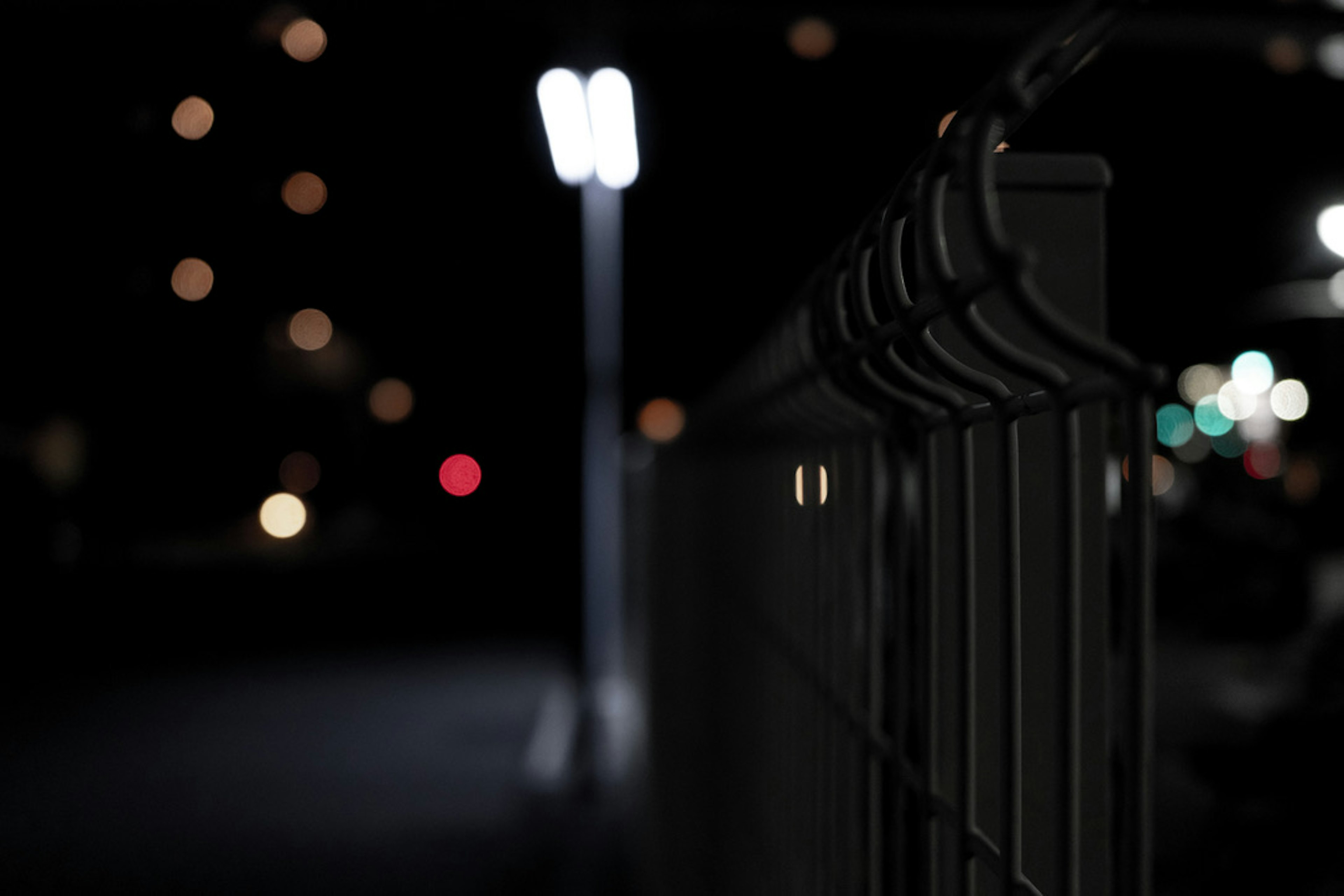 Close-up of a fence at night with streetlights and blurred background