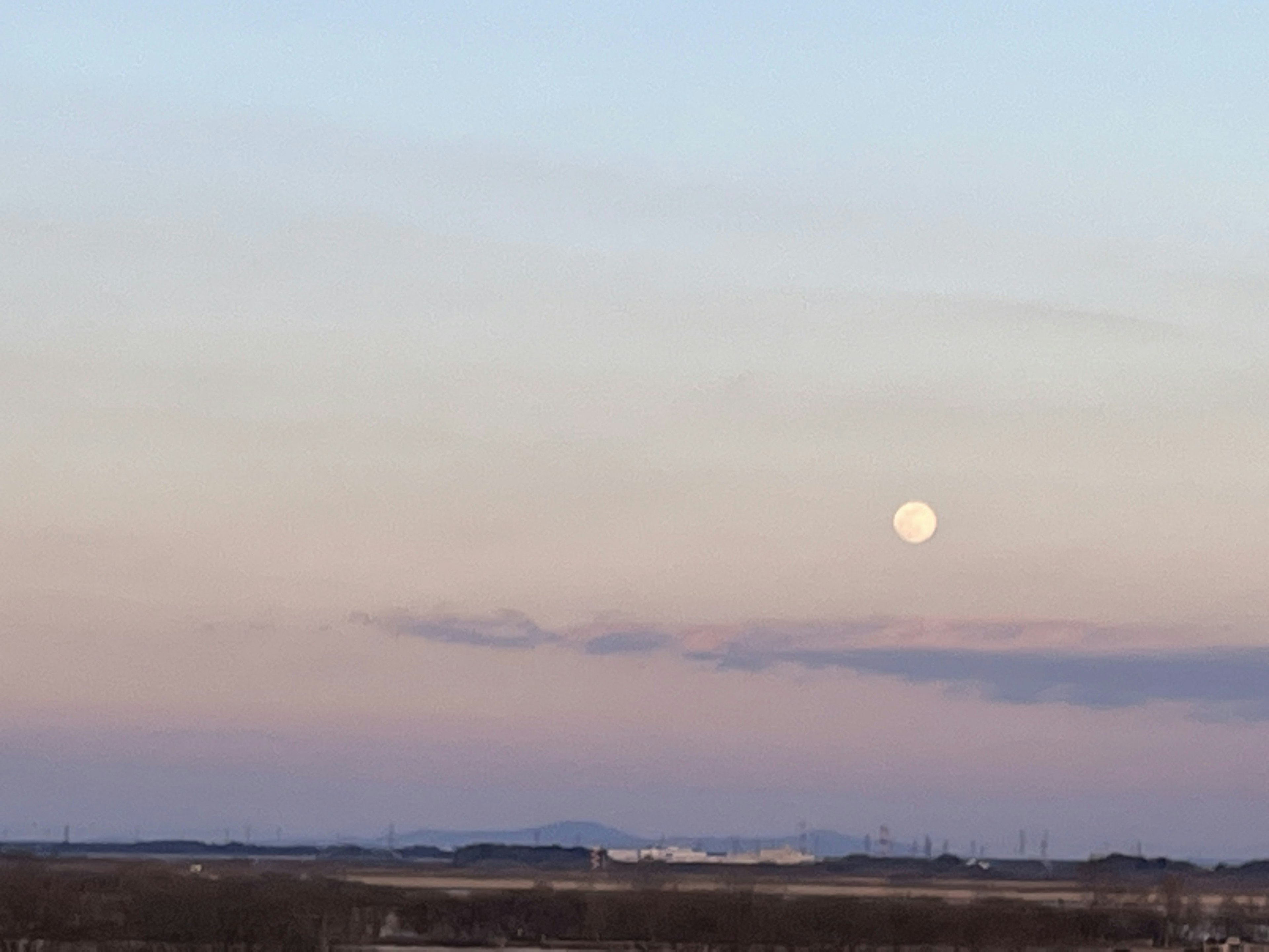 Moon rising in a pastel sky with soft pink clouds at dusk