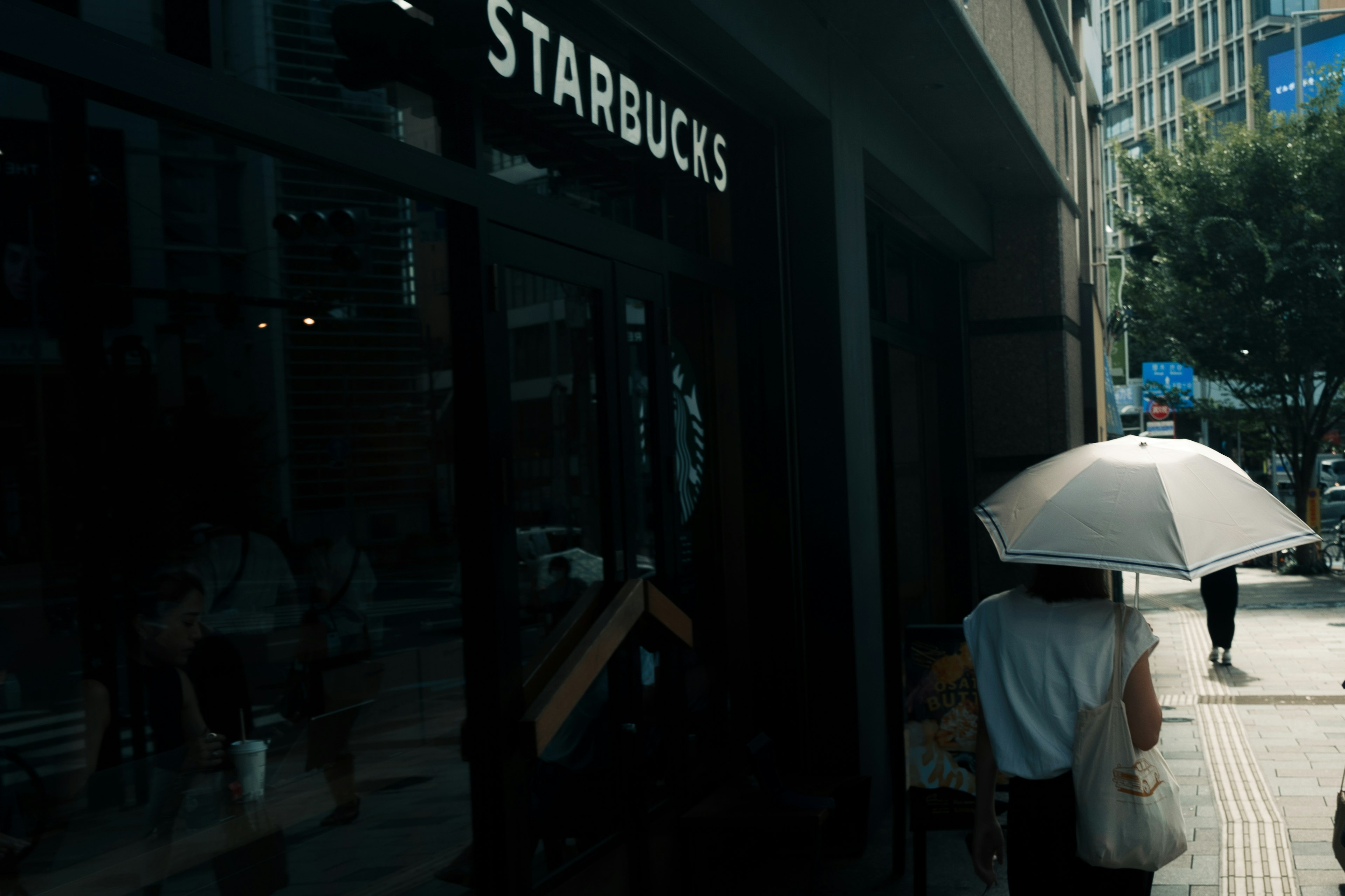 Một người đang đi bộ trên đường với biển hiệu Starbucks và ô che nắng