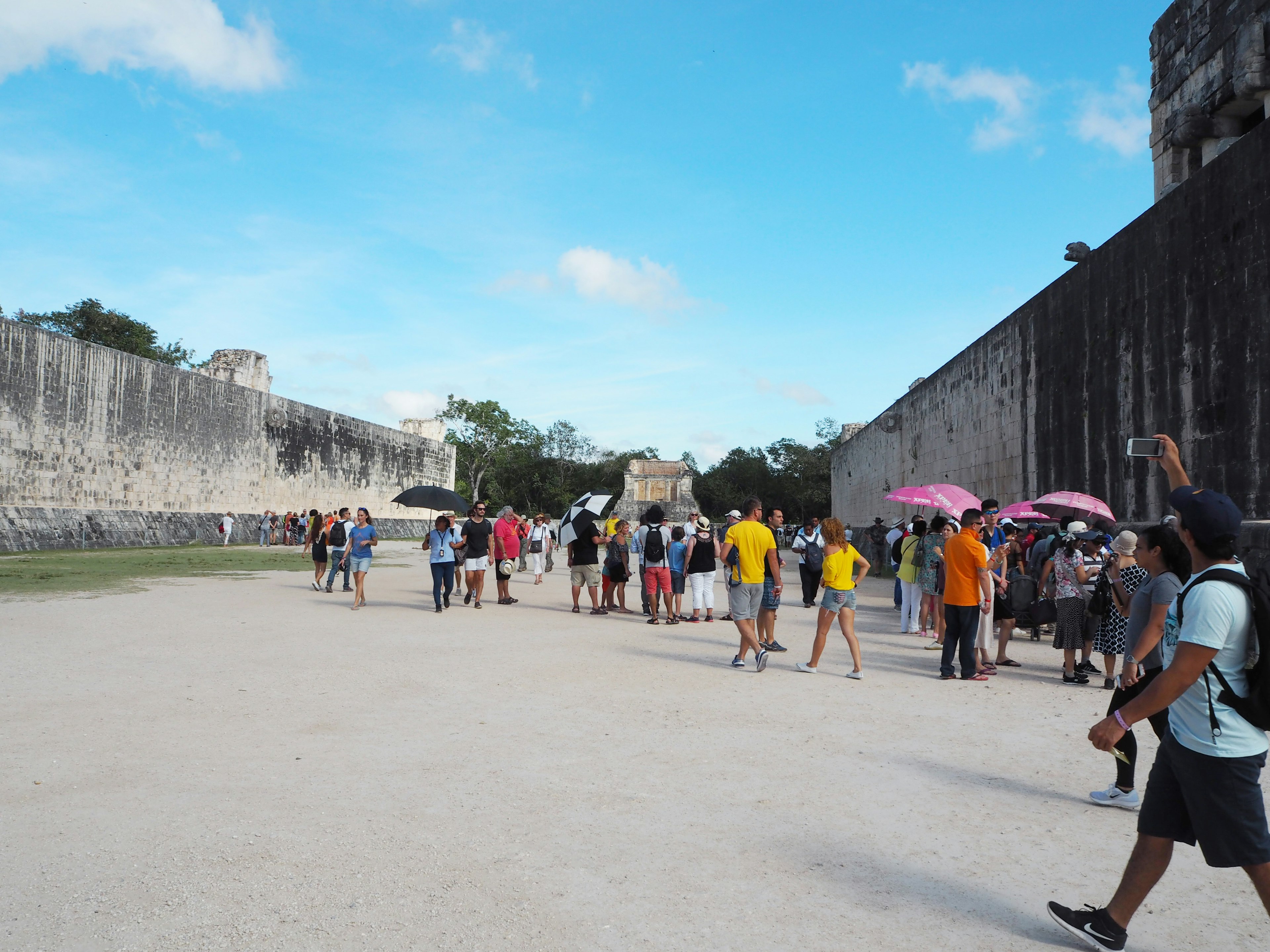 Crowd of tourists visiting Chichen Itza ruins with umbrellas under a blue sky