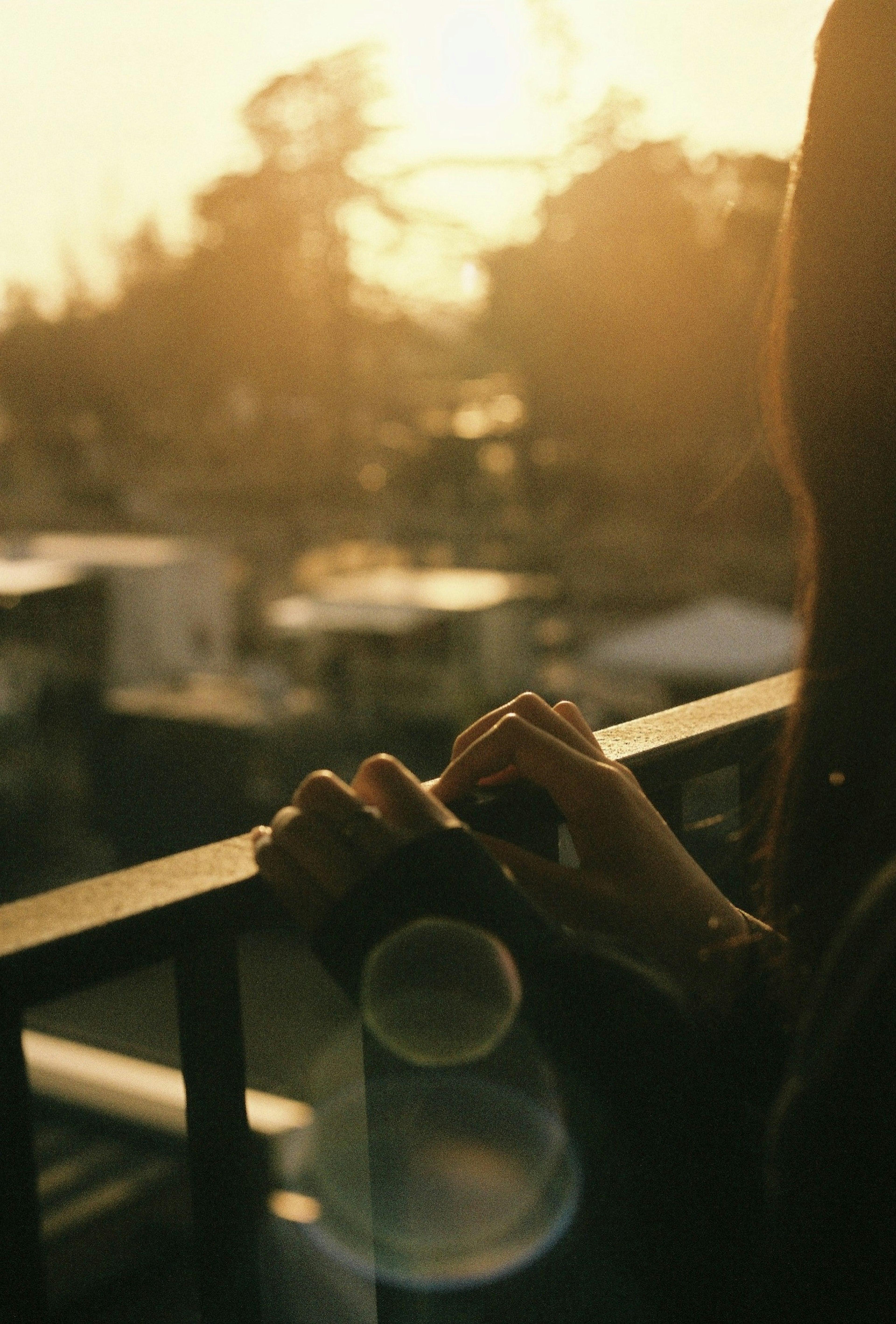 Mains reposant sur une balustrade de balcon illuminées par la lumière du coucher de soleil