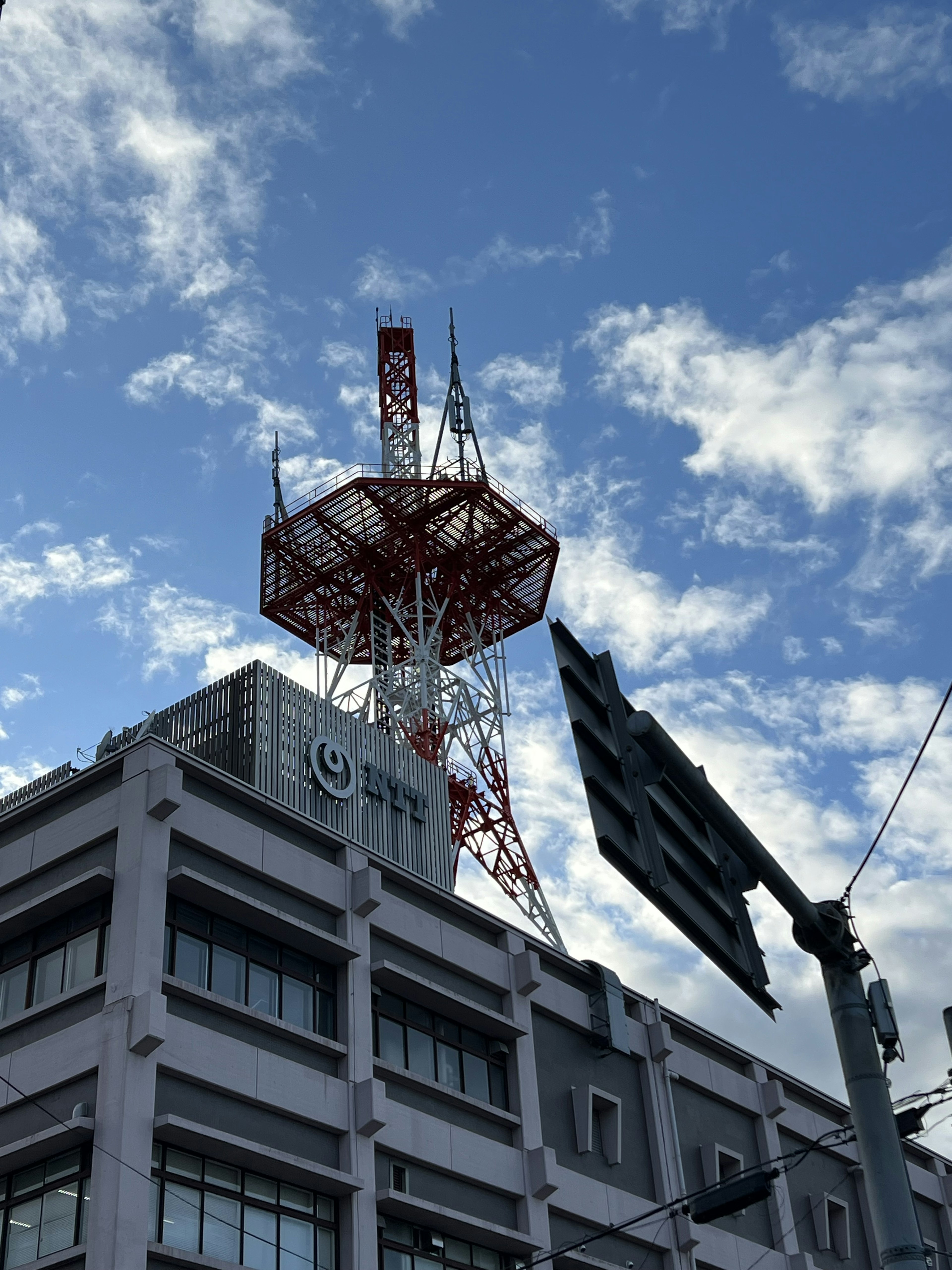 Menara komunikasi merah dan putih menjulang di atas gedung di bawah langit biru