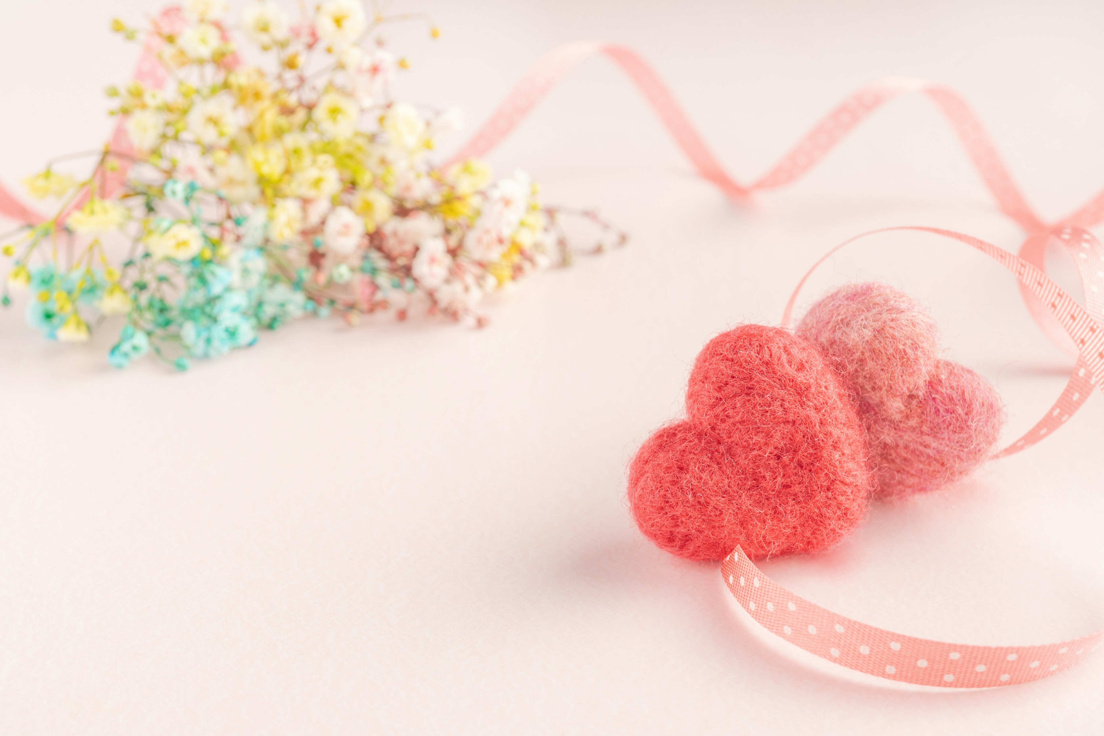 Pink felt heart decorations with colorful flowers in the background