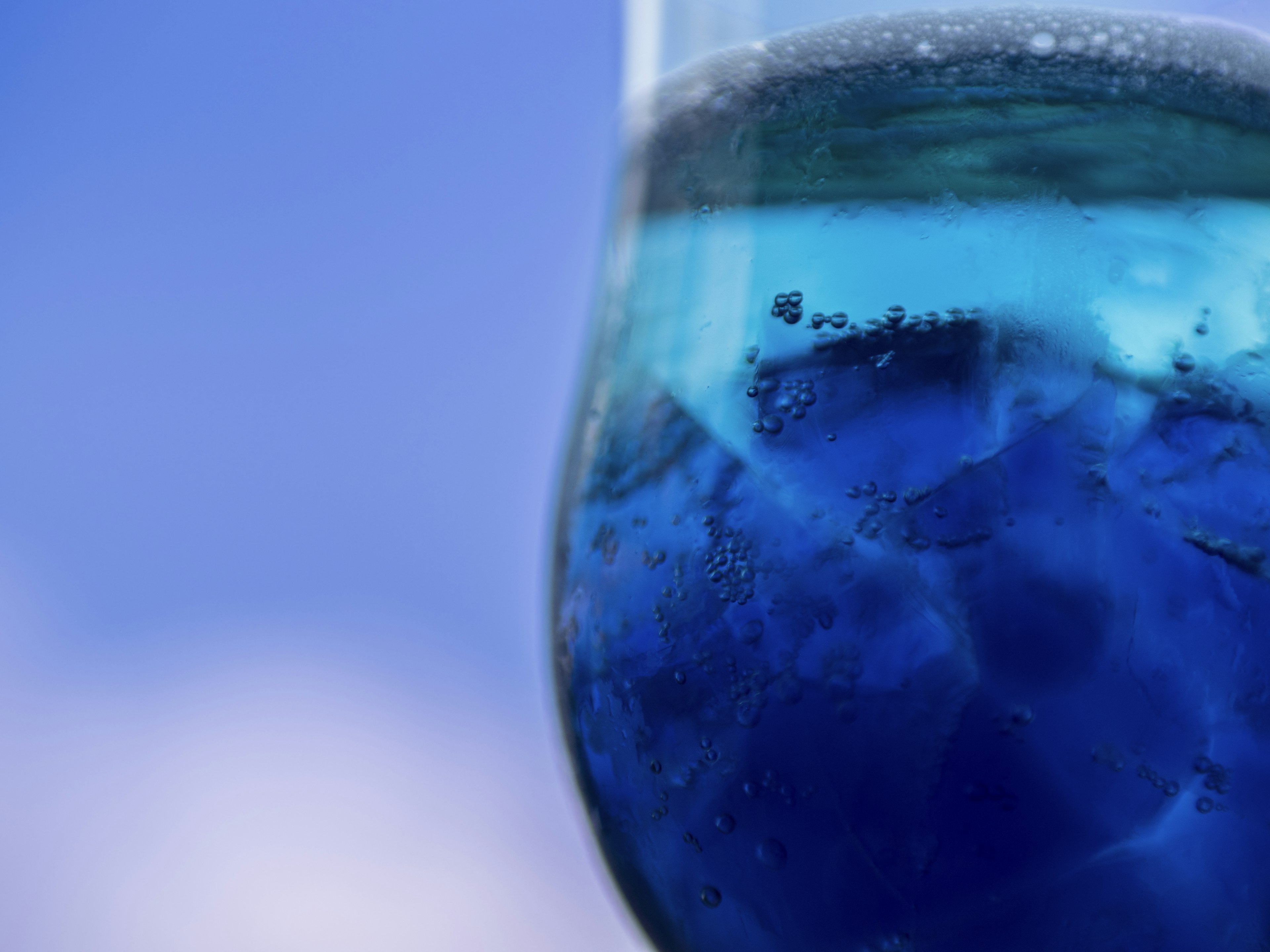 Primo piano di un bicchiere con liquido blu su sfondo di cielo blu