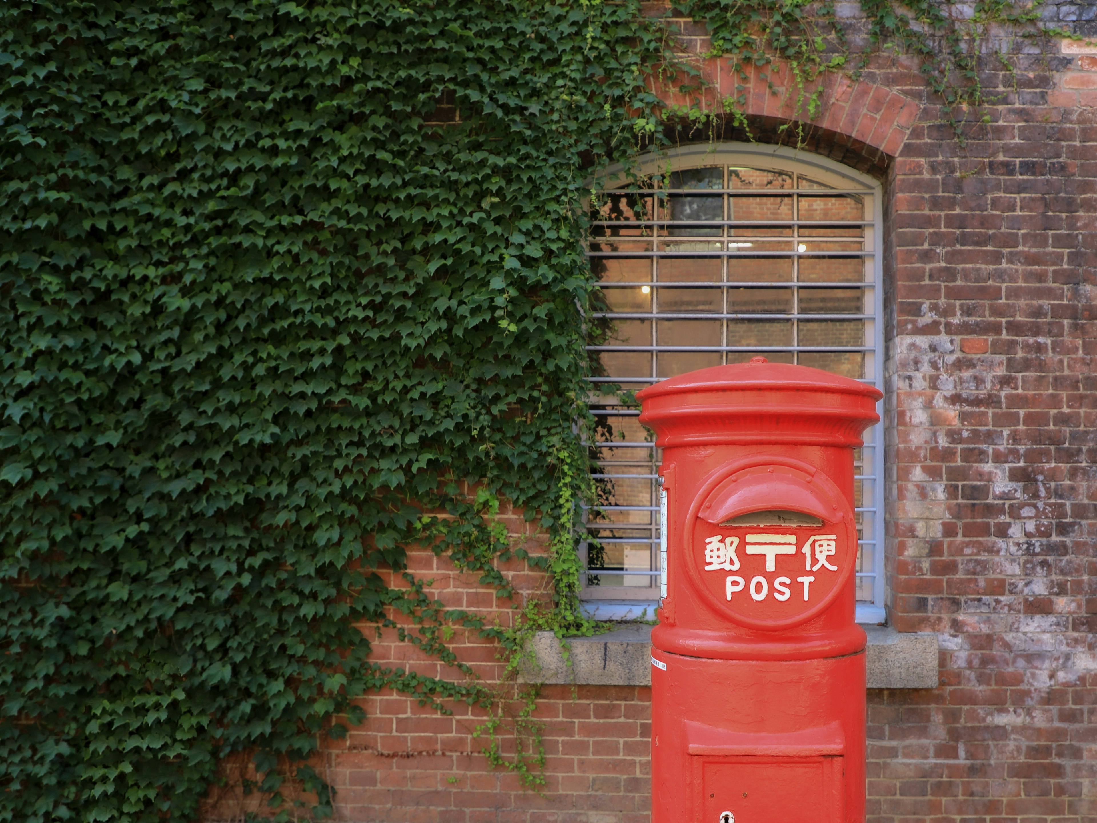 Red post box with green ivy on a brick wall