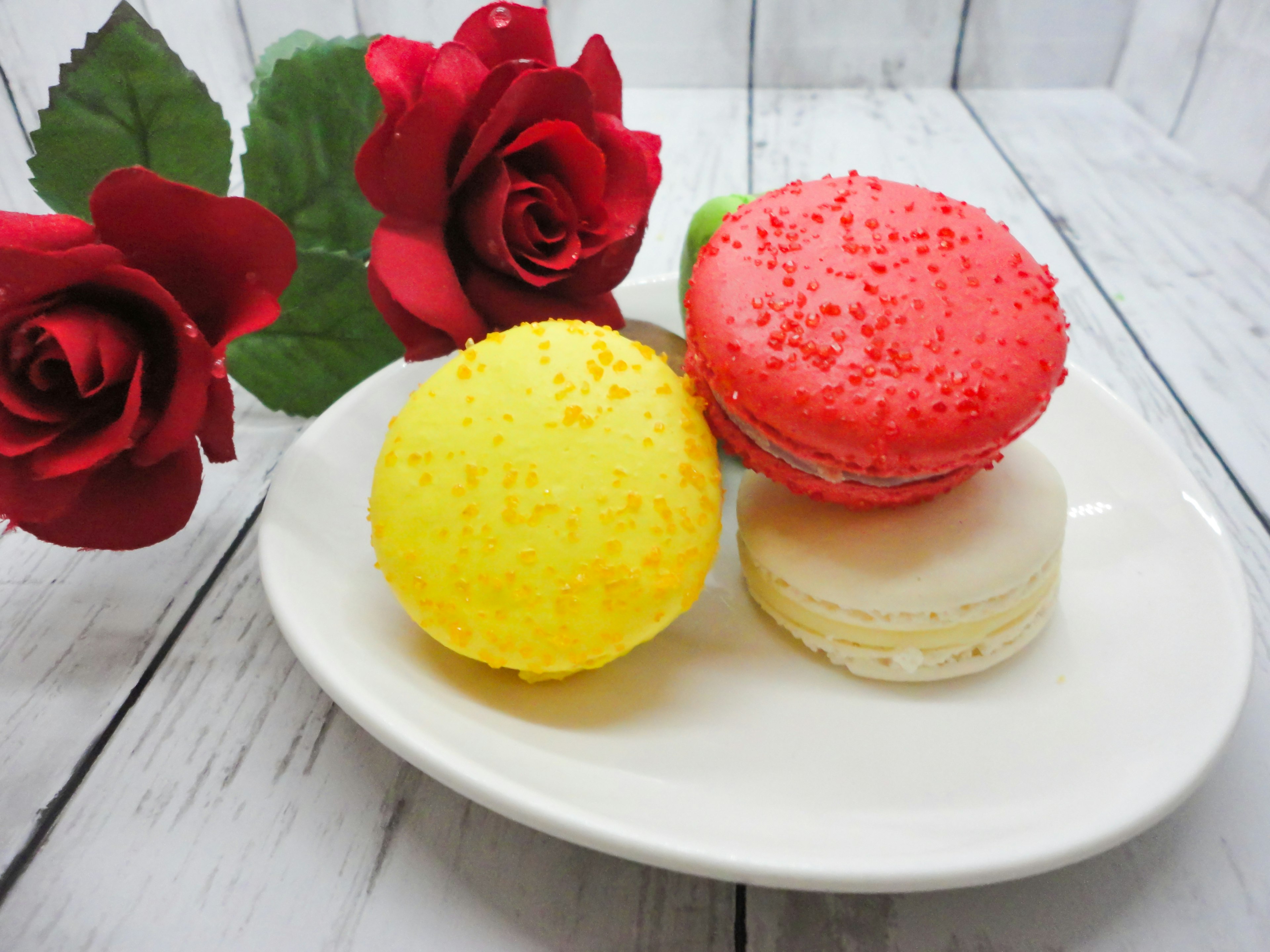 Une assiette avec des macarons colorés et des roses rouges