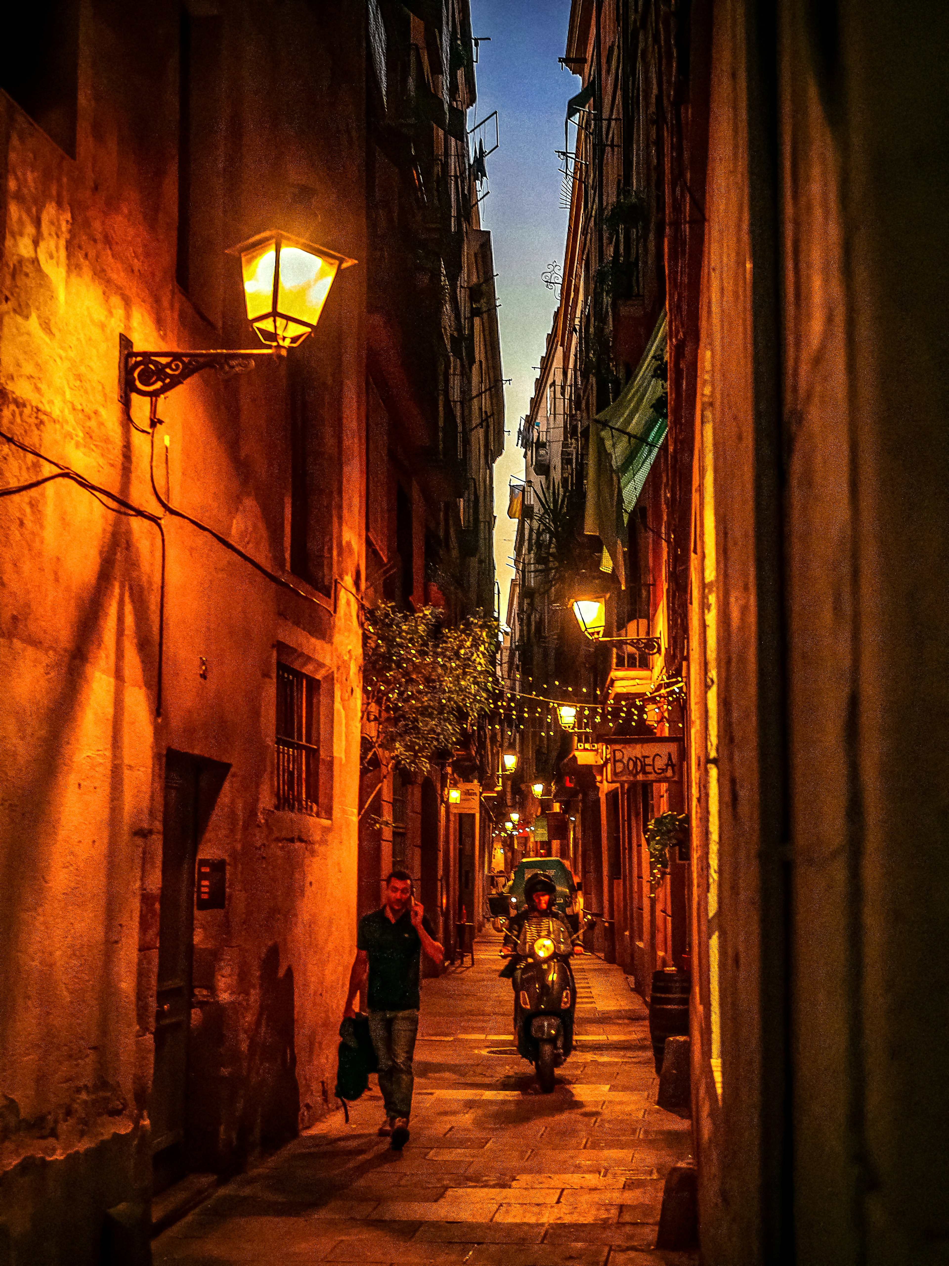 Narrow alleyway at dusk with orange streetlights and a motorcycle