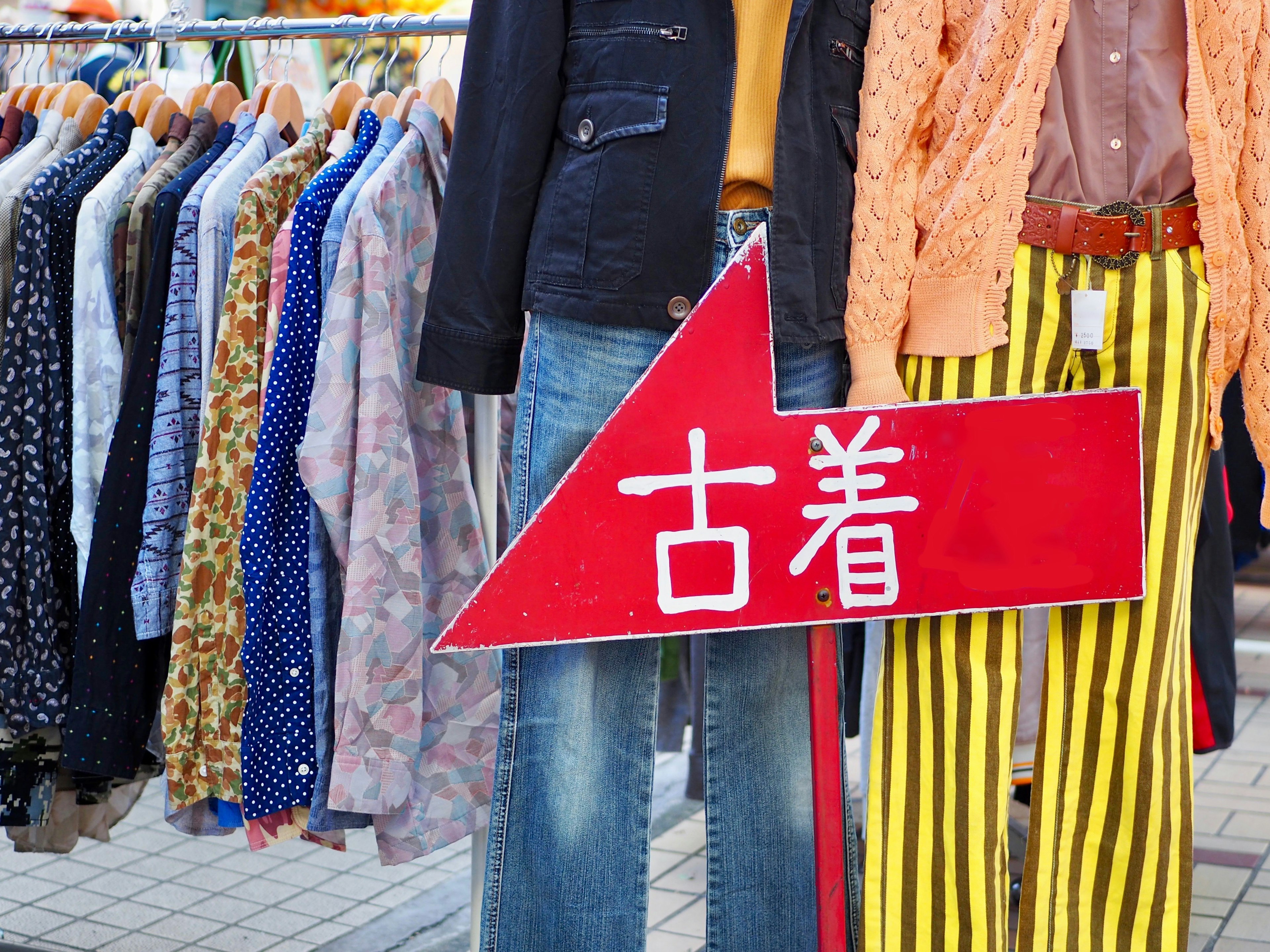 Scena di mercato con abbigliamento vintage e un cartello che indica abiti di seconda mano