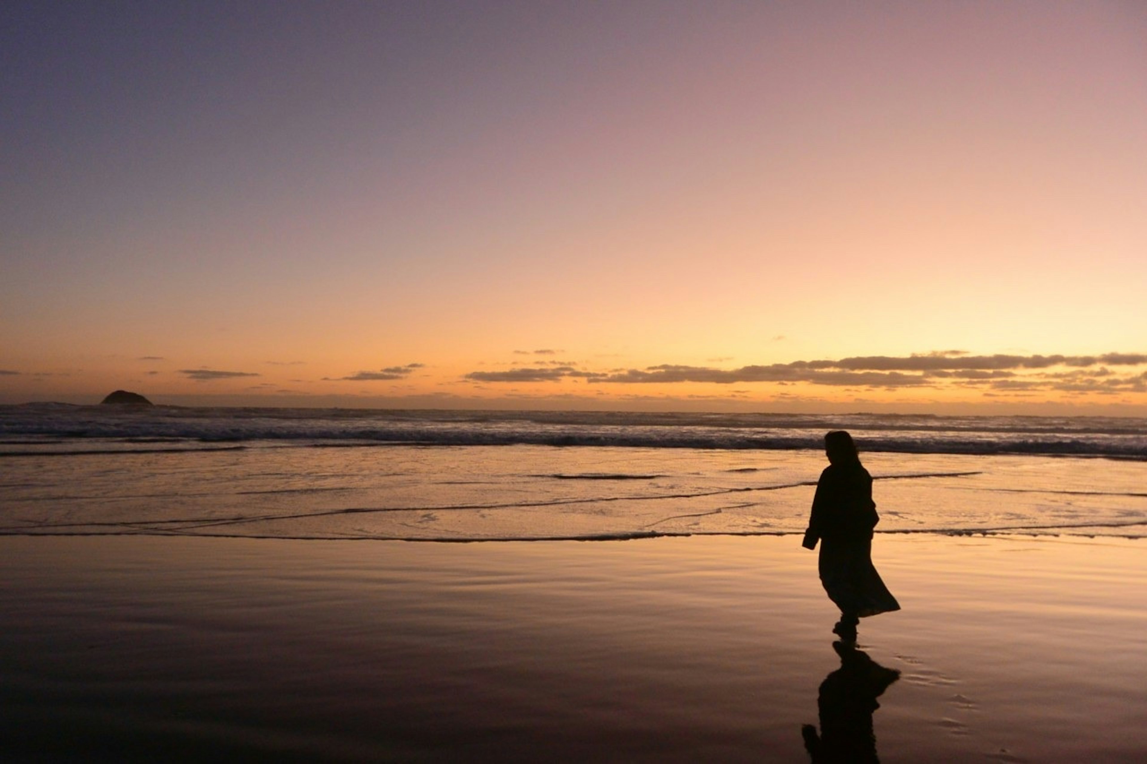 Silhouette d'une personne marchant le long d'une plage au coucher du soleil