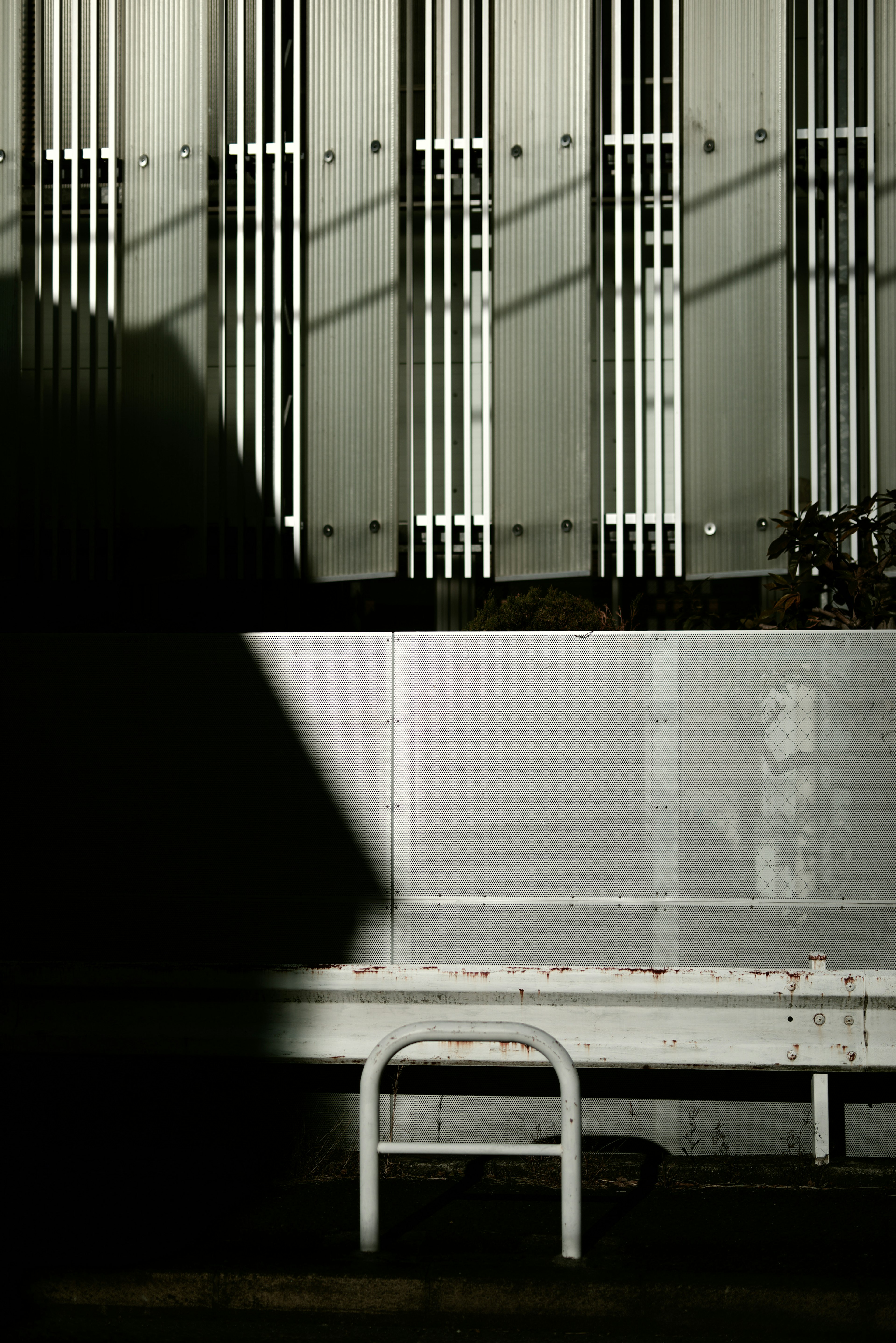 Mur en métal ombragé avec des lignes verticales et un banc blanc