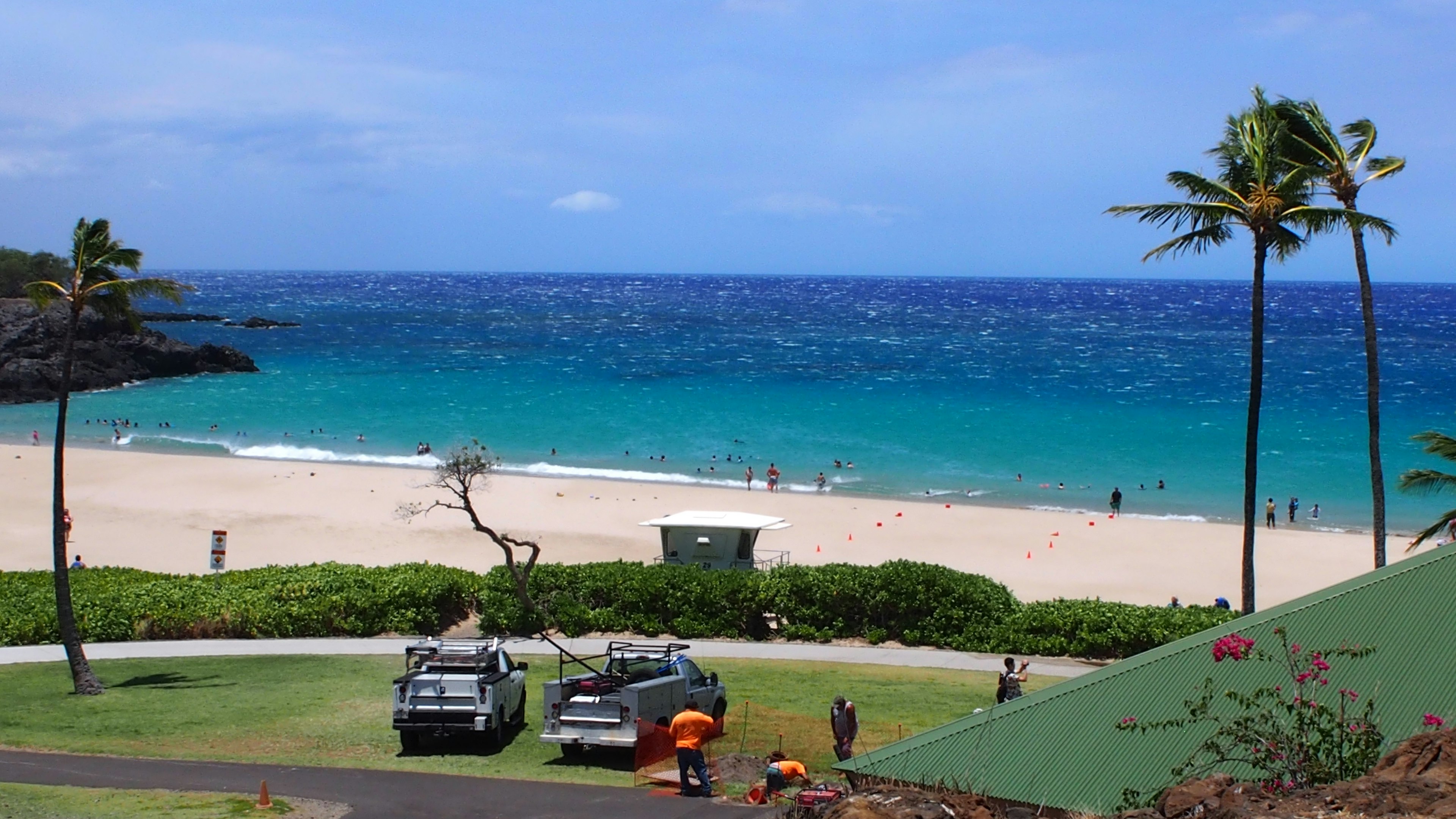 Vue panoramique de l'océan bleu et de la plage de sable blanc avec des voitures garées devant une pelouse verte